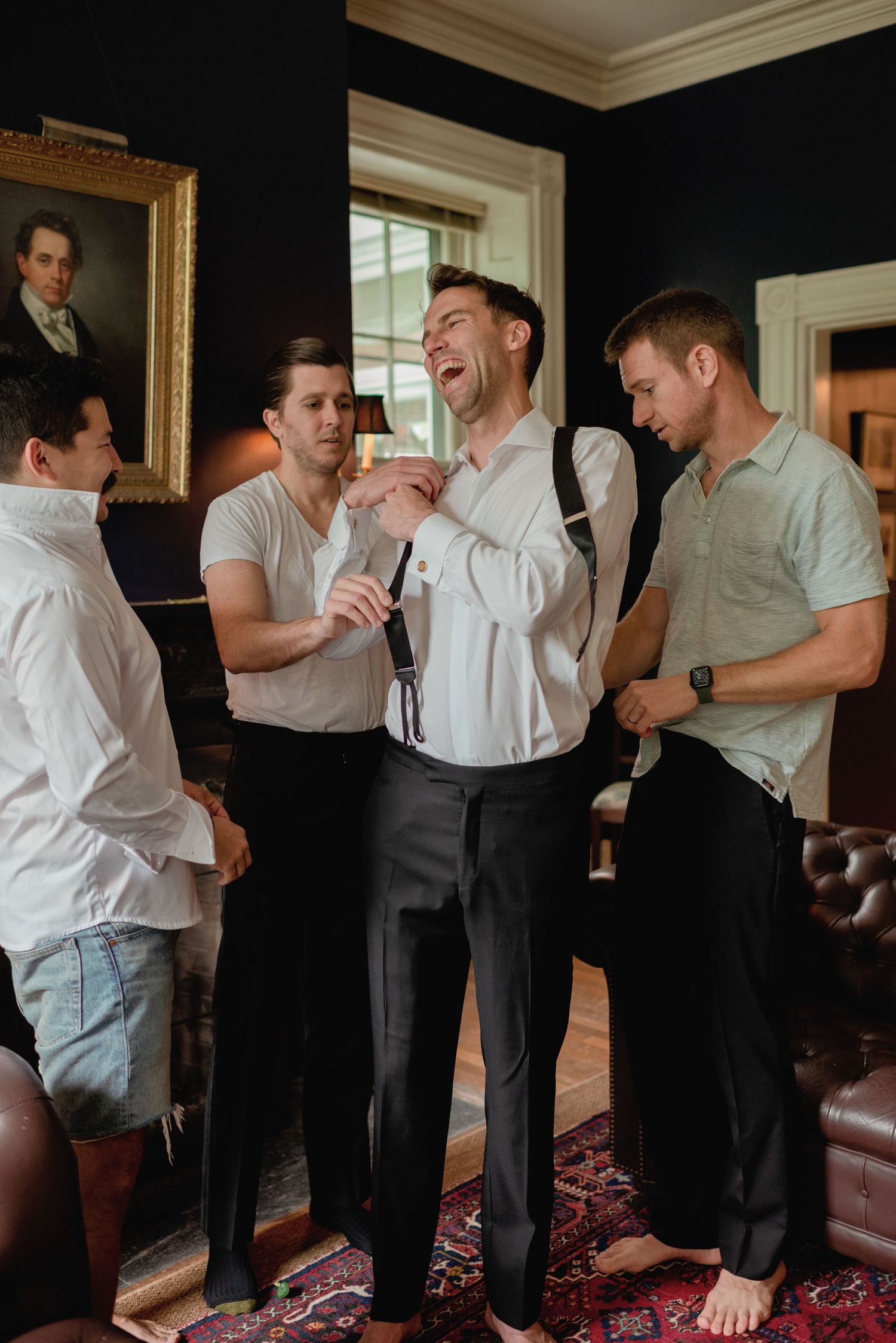 Groomsmen sharing laughs and drinks while getting ready in formal attire.