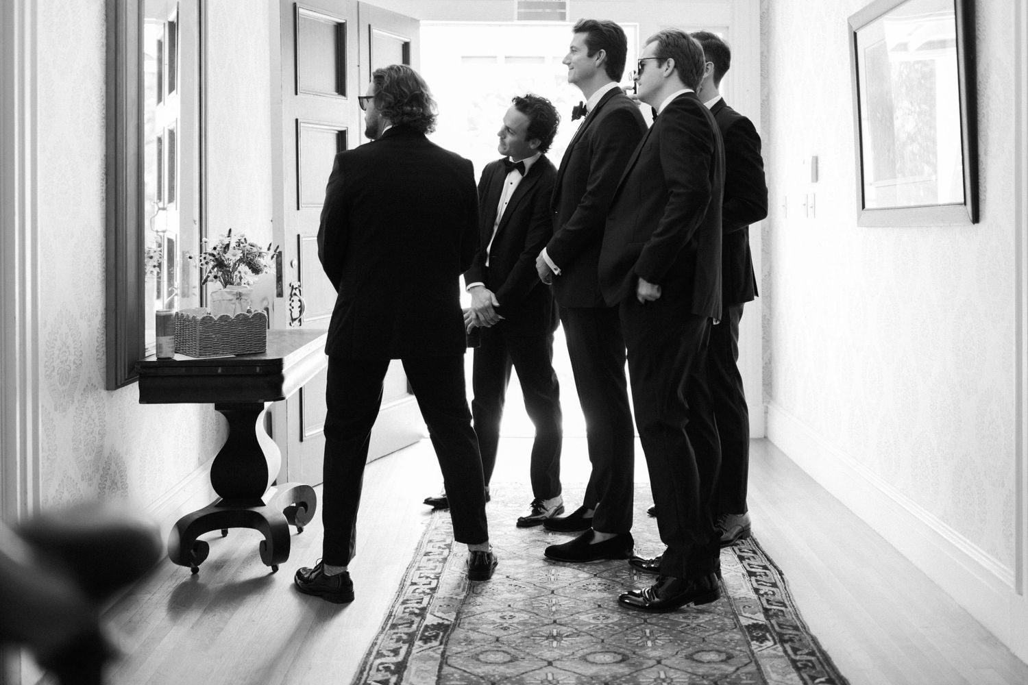 Wedding party members in formal attire gather in a hallway before the ceremony.