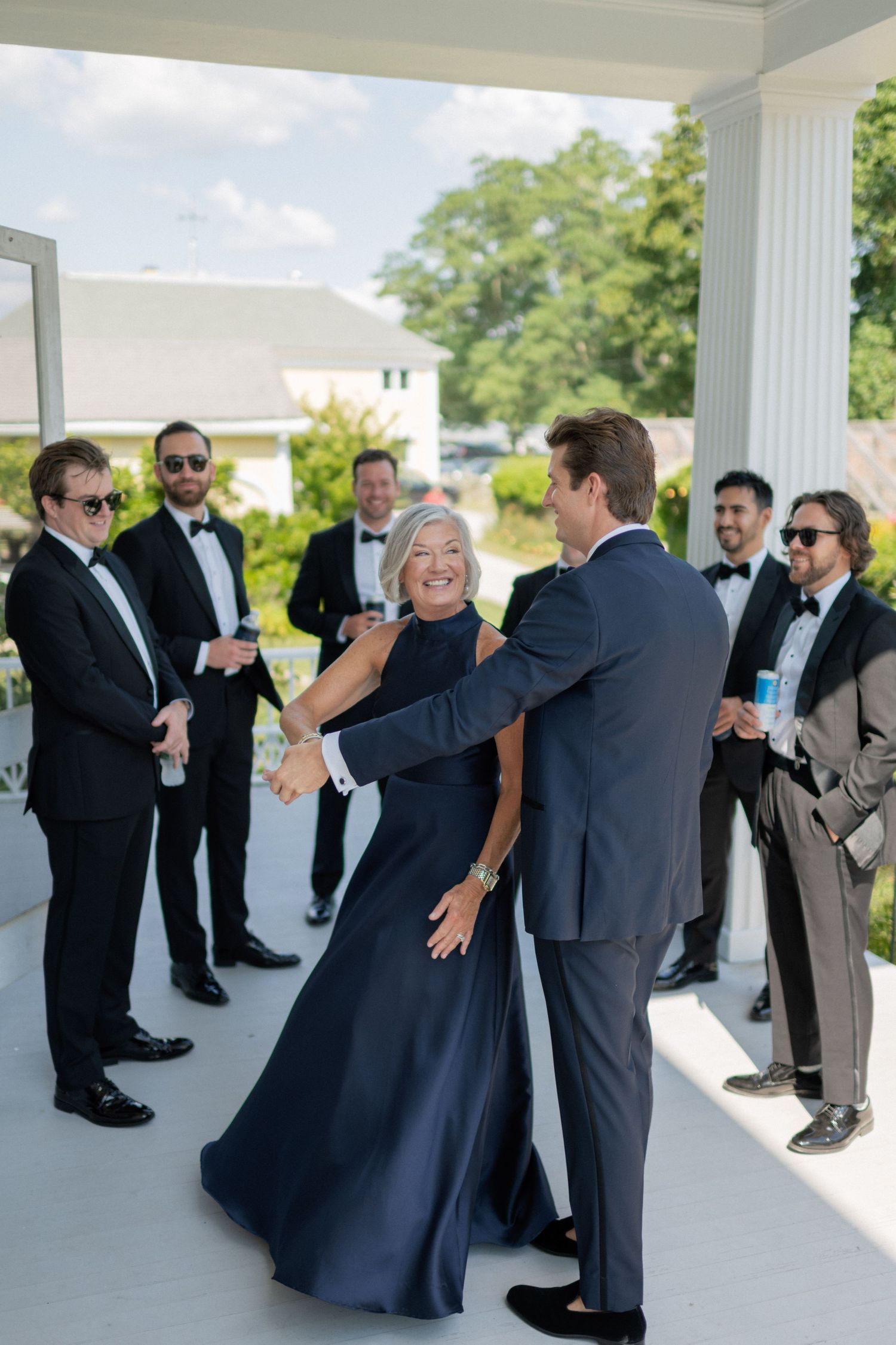 Wedding party members celebrate with a joyful dance moment on an outdoor porch.