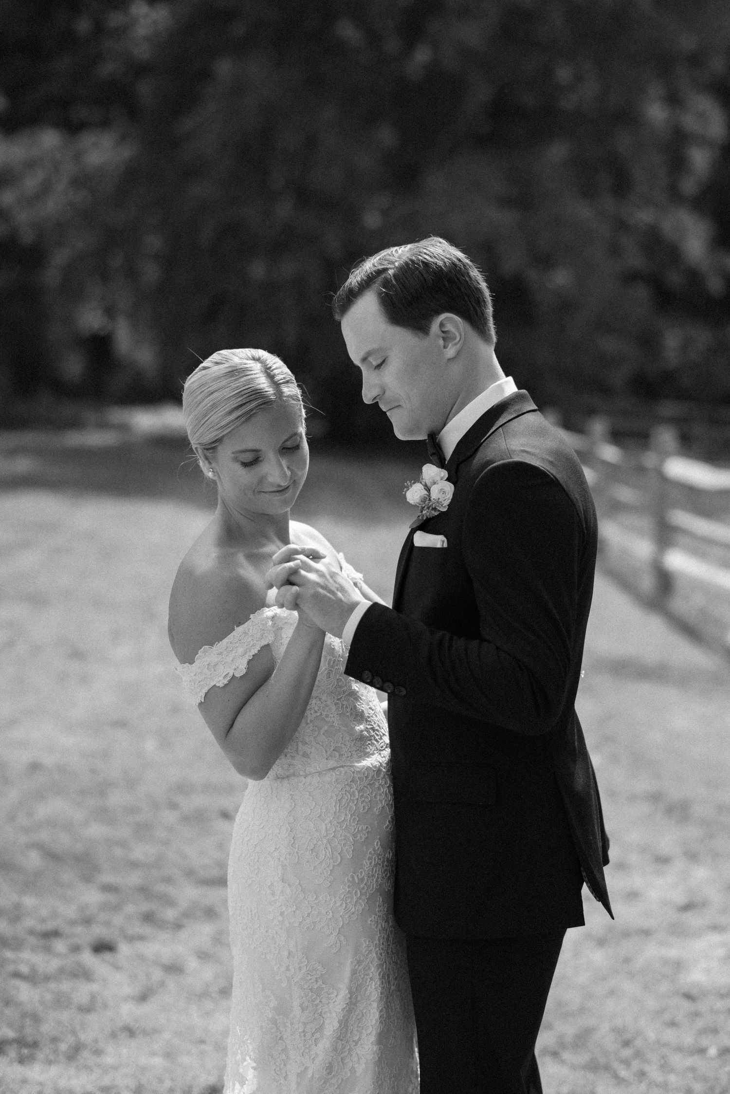 Black and white photo of couple exchanging rings during outdoor wedding ceremony.