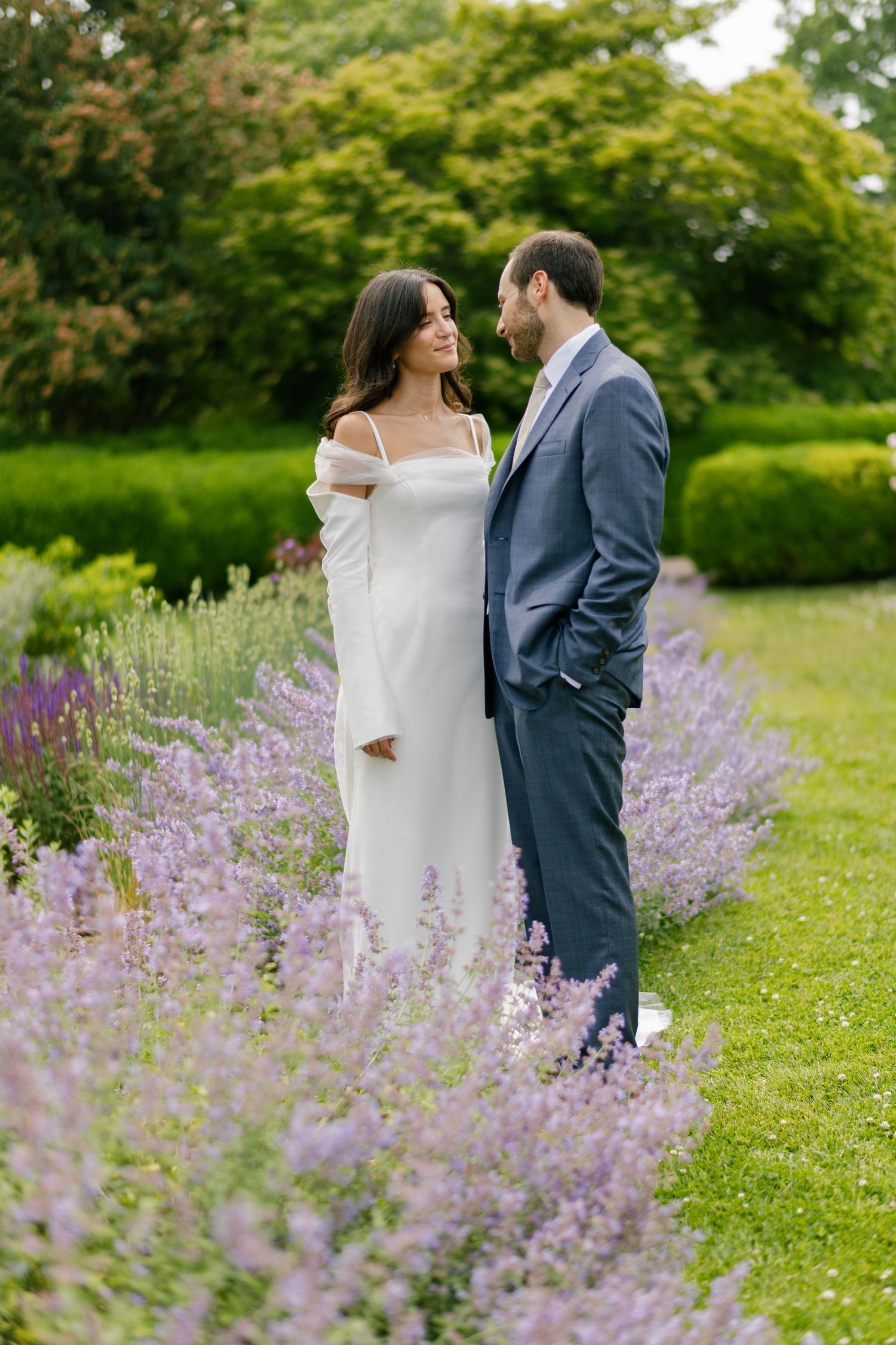 A romantic couple stands together in a garden with blooming purple lavender flowers in the foreground.
