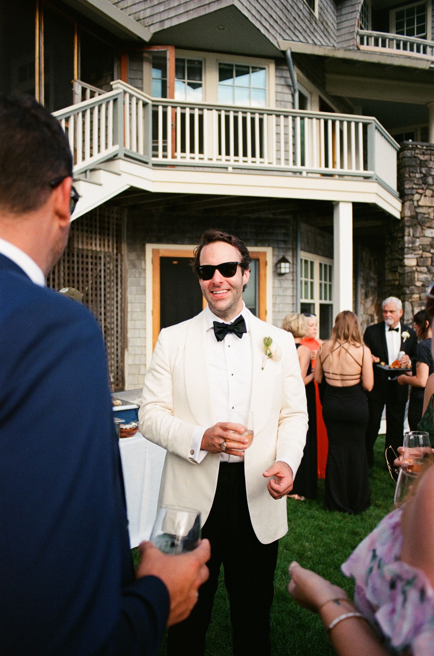 Outdoor social event with guests in formal attire mingling on a lawn.