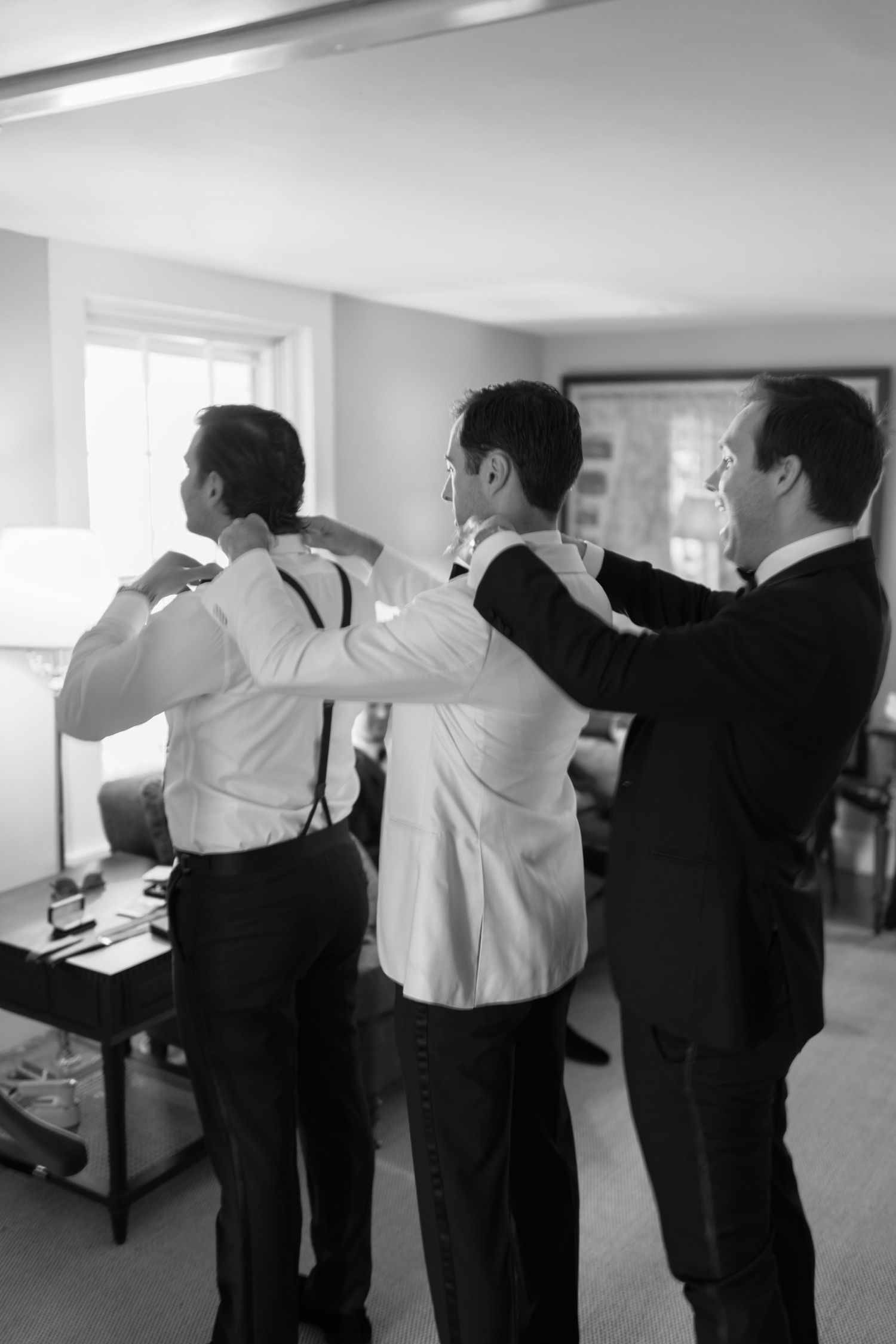 Black and white photo of groomsmen helping each other get ready before the wedding.