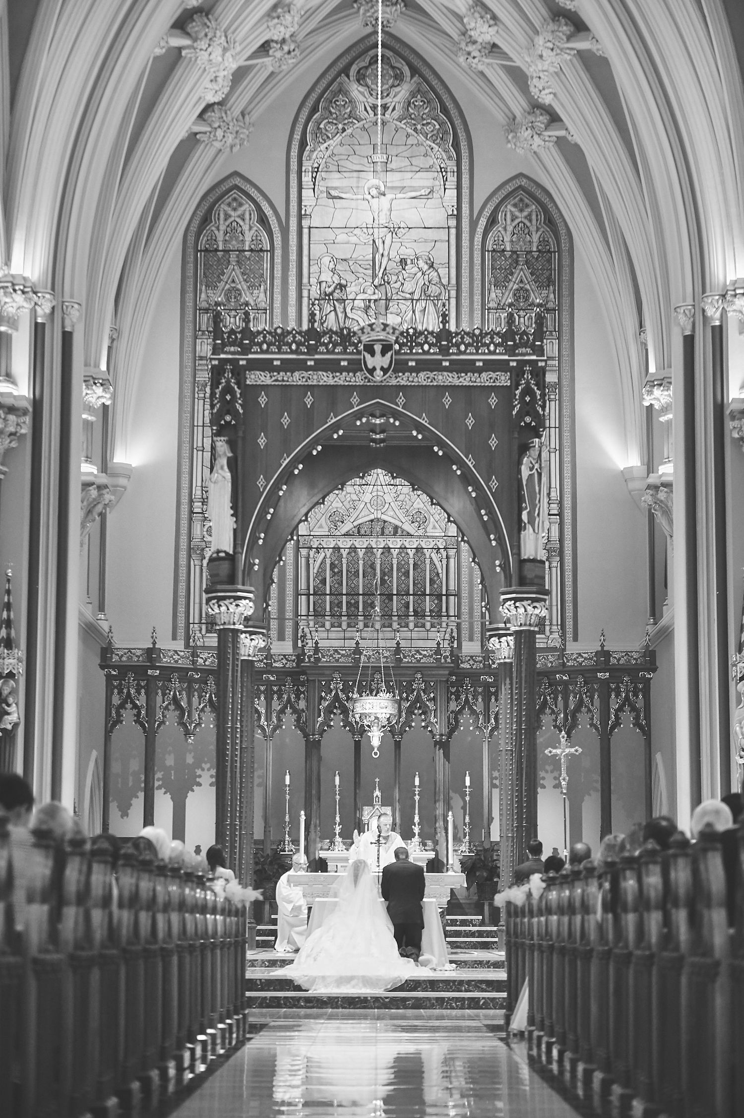 Black and white photo of wedding ceremony in grand Gothic cathedral with ornate altar and architecture.