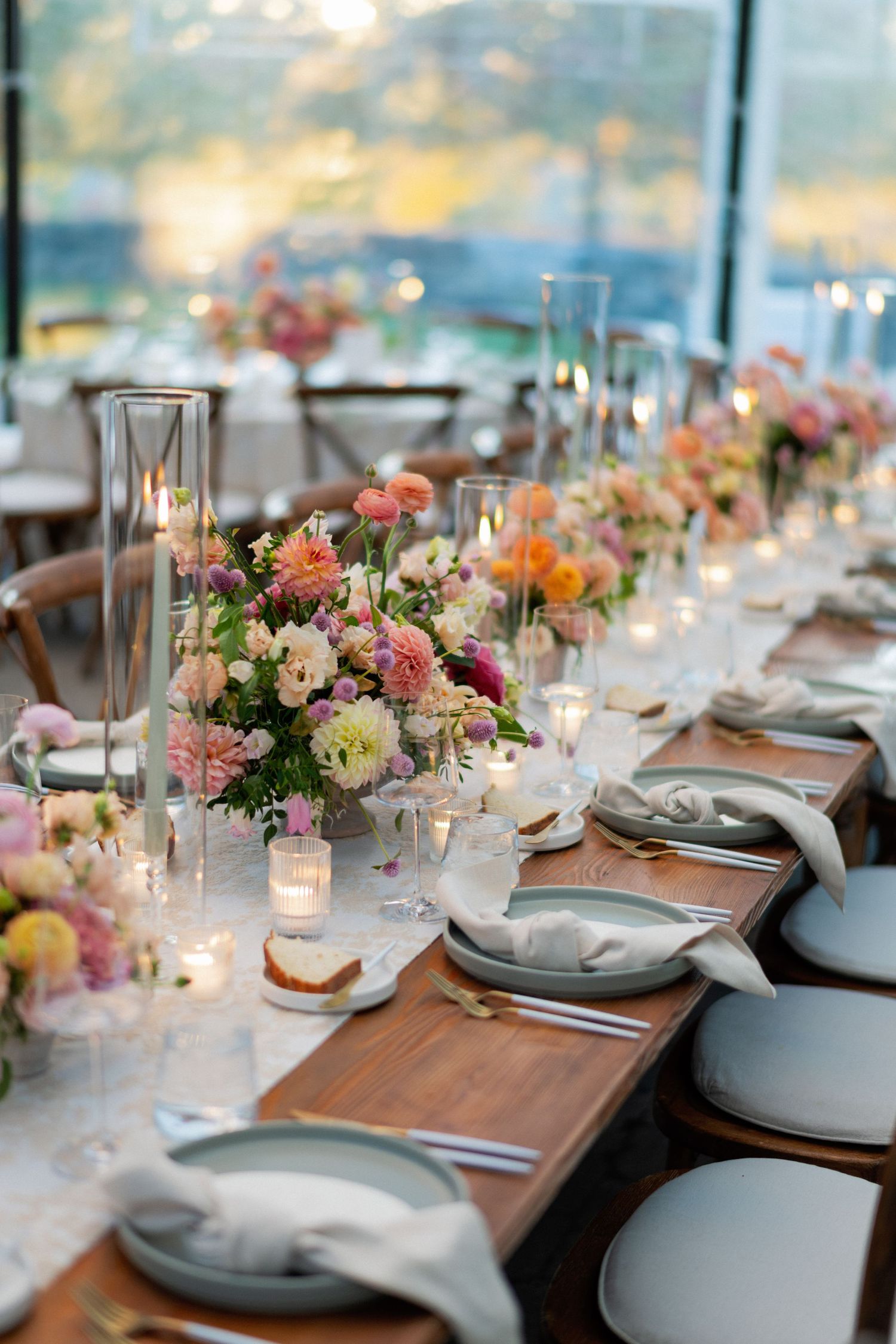 Elegant wedding reception table setting with pink floral centerpieces, glassware, and place settings at sunset.