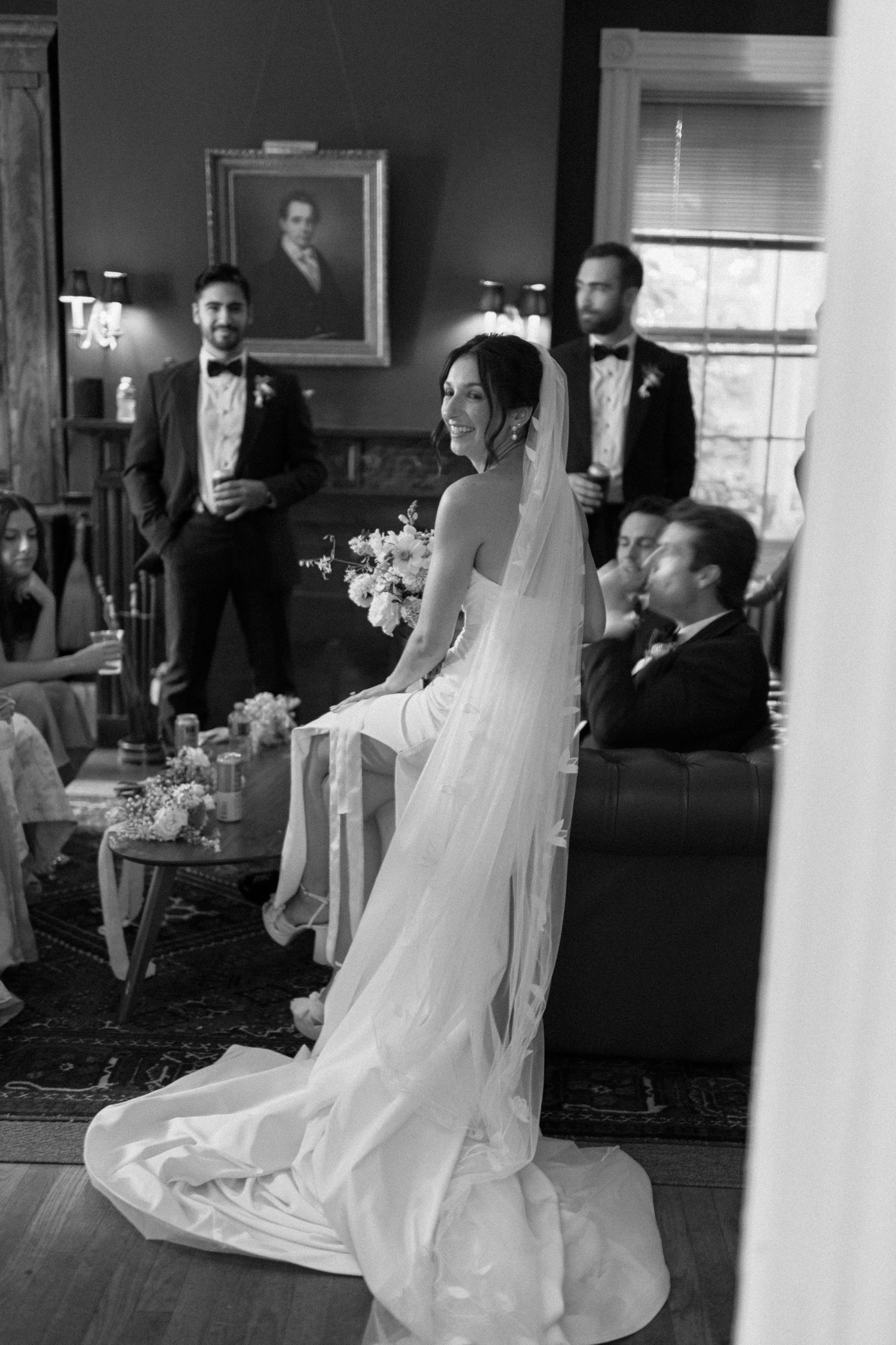 Elegant wedding scene in vintage room with dramatic flowing veil and formal attire.