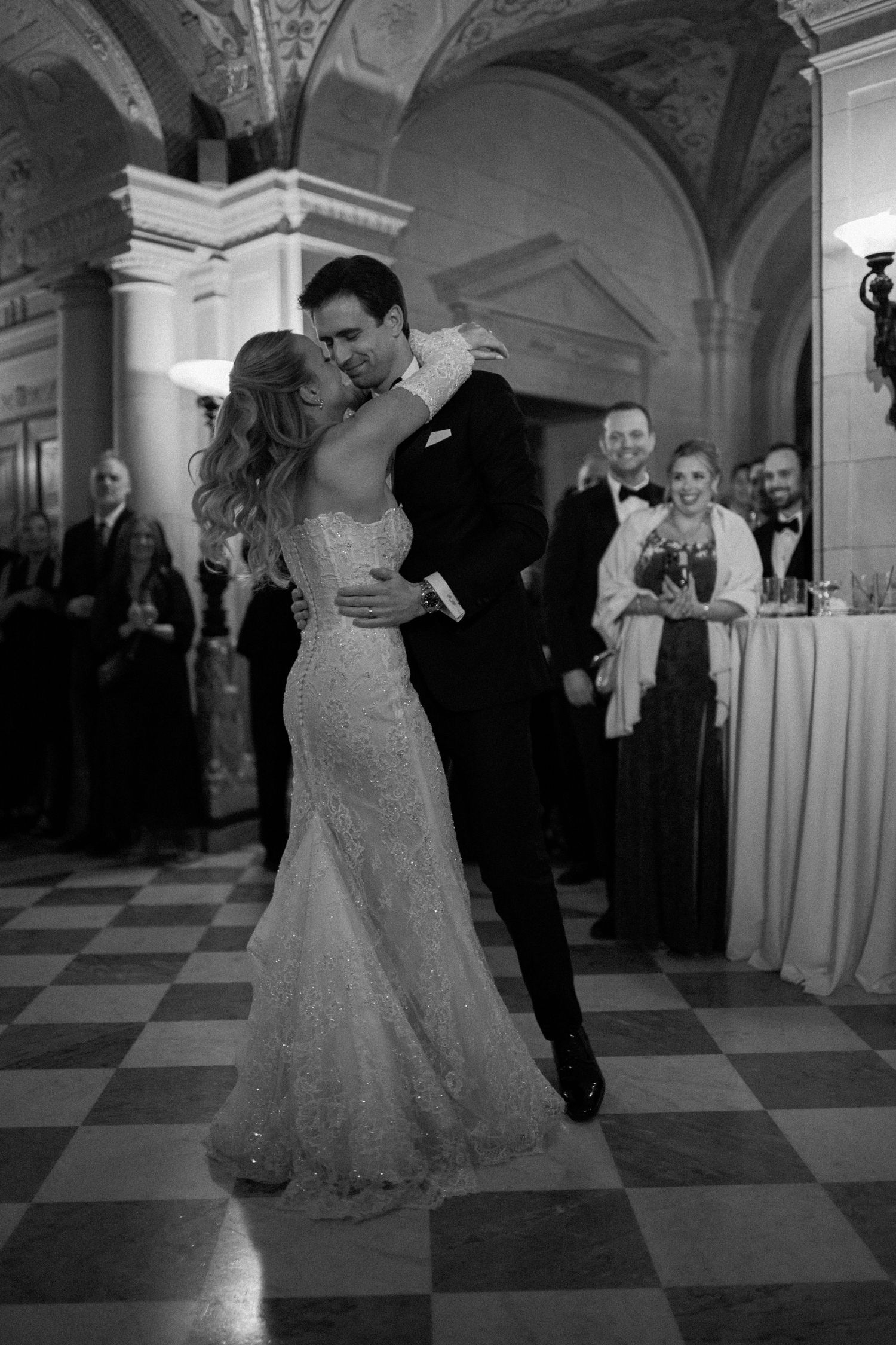 Newlyweds share their first dance on a black and white checkered ballroom floor at an elegant wedding reception.