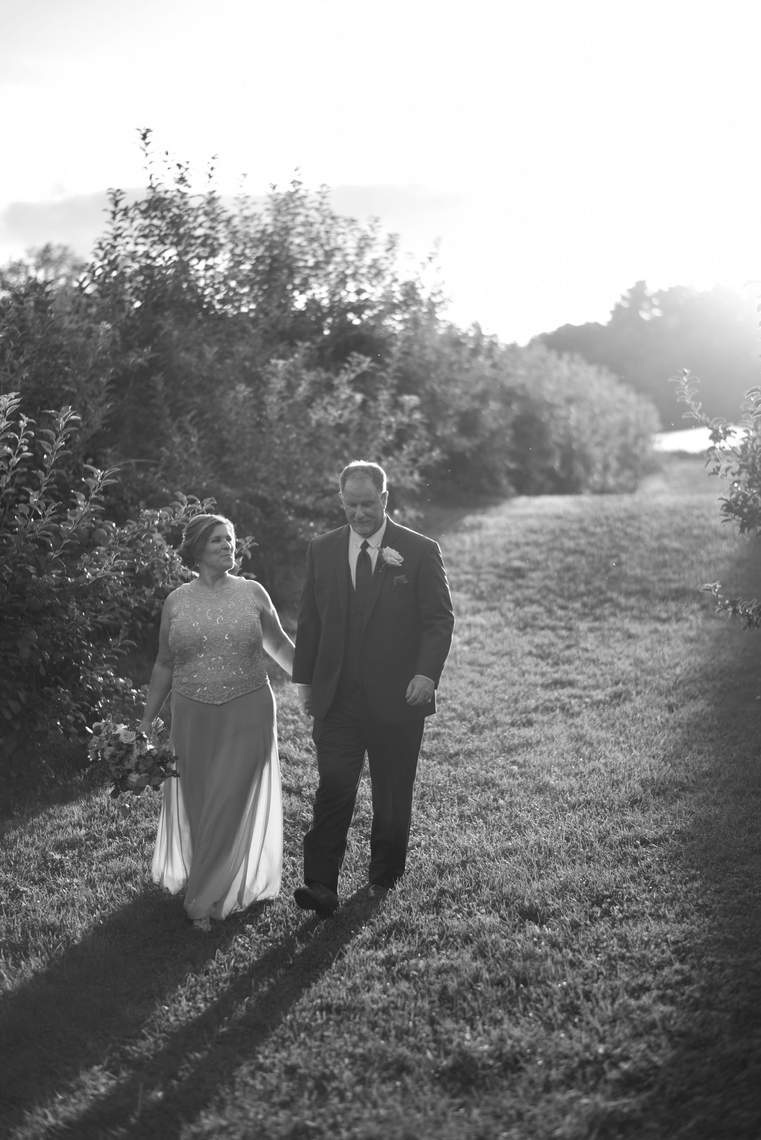 Black and white photo of couple walking together on hillside path during sunset.