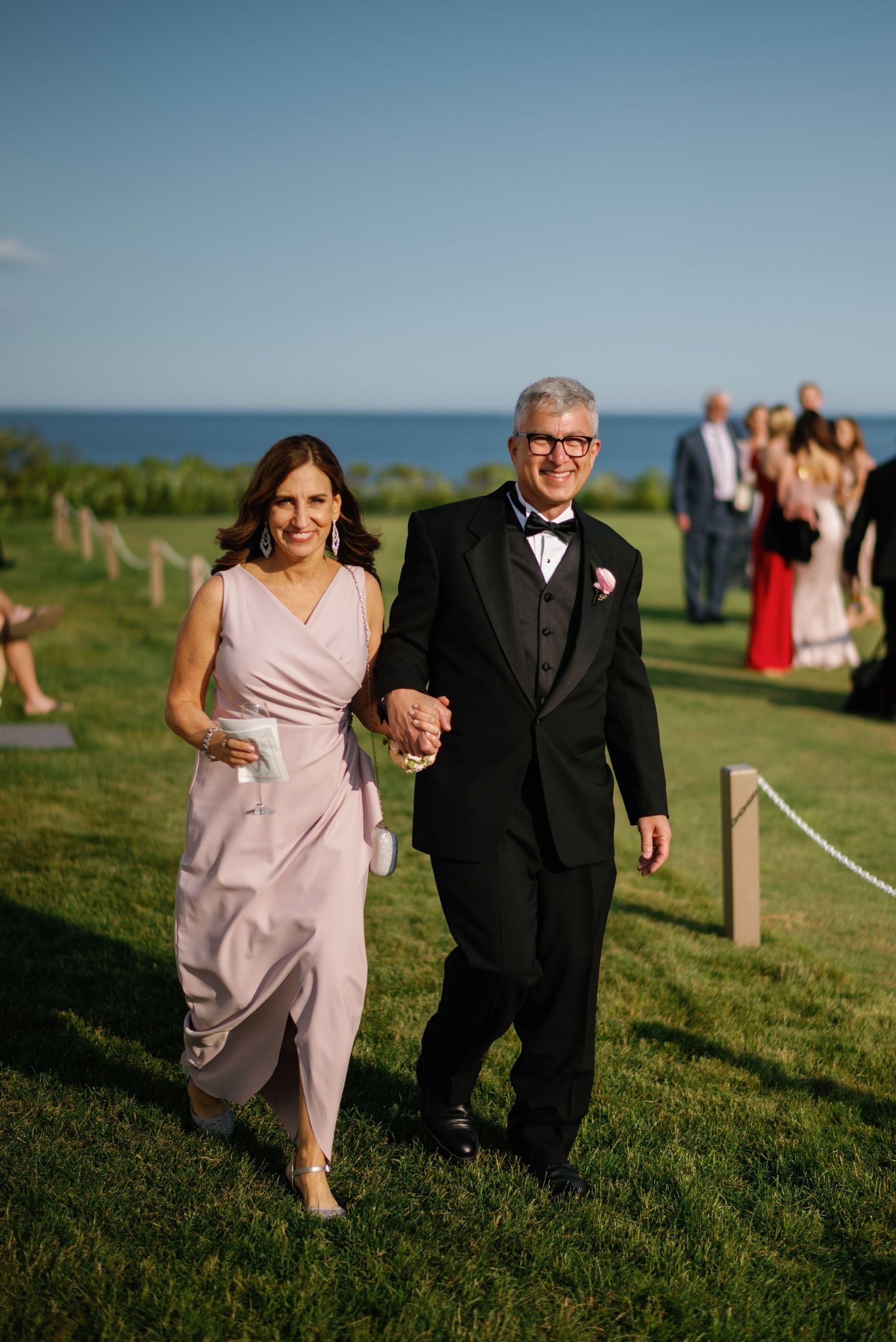 A couple in formal attire walks together on a green lawn during an outdoor event.