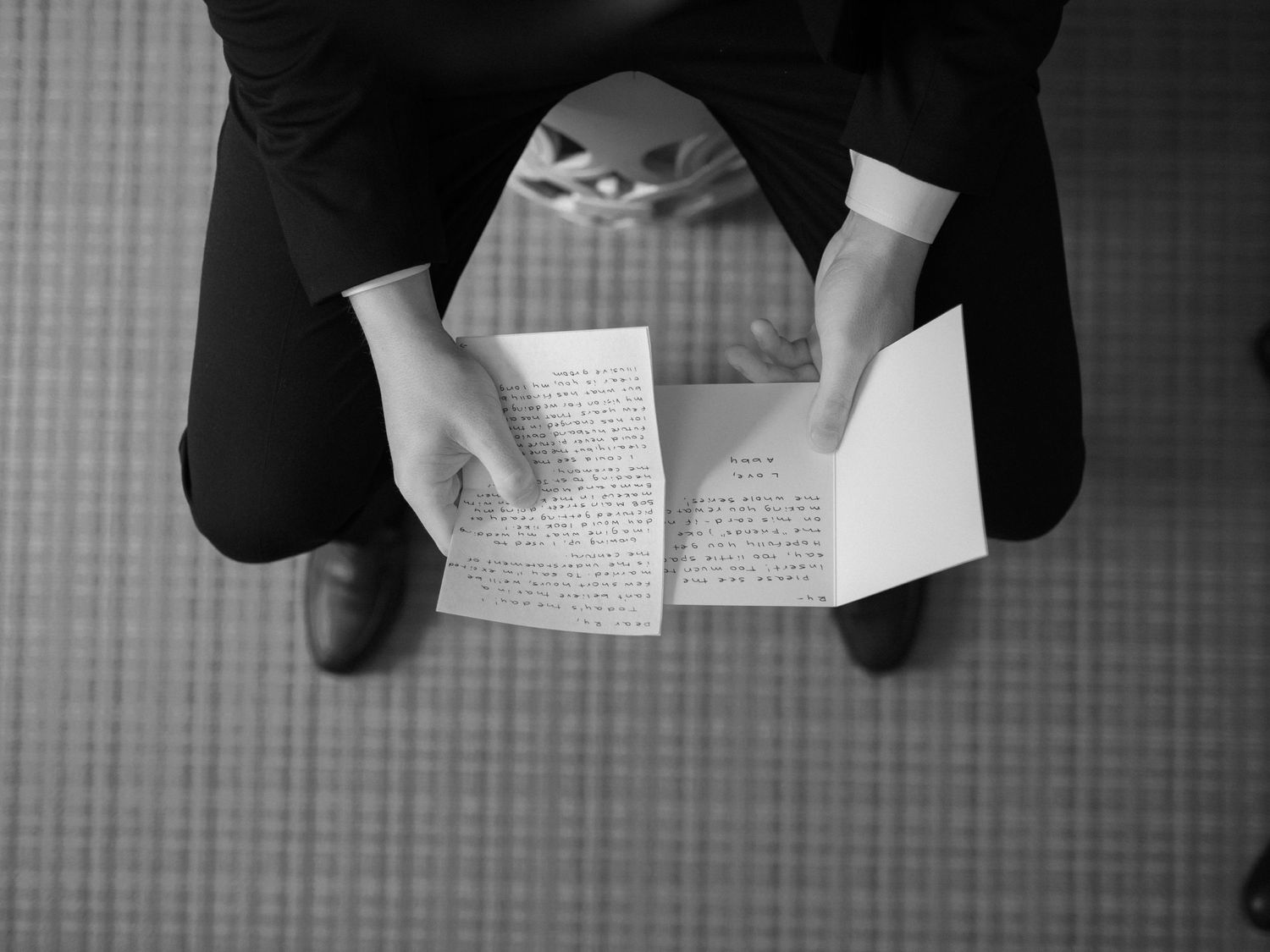 Overhead black and white view of person reading or writing in book on patterned floor.