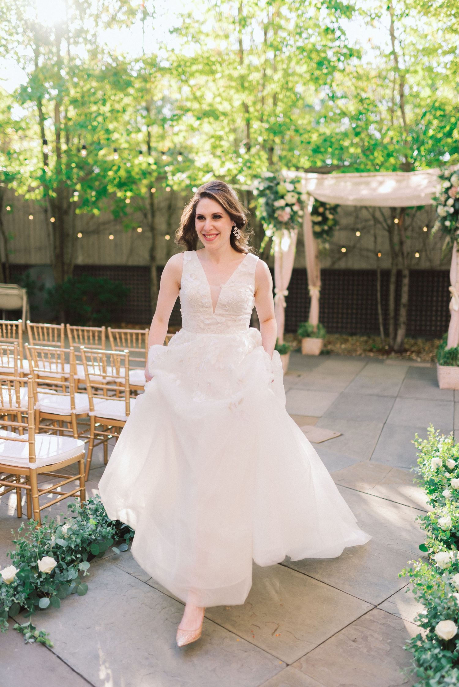 A bride in an elegant white wedding gown poses in a garden setting with string lights.