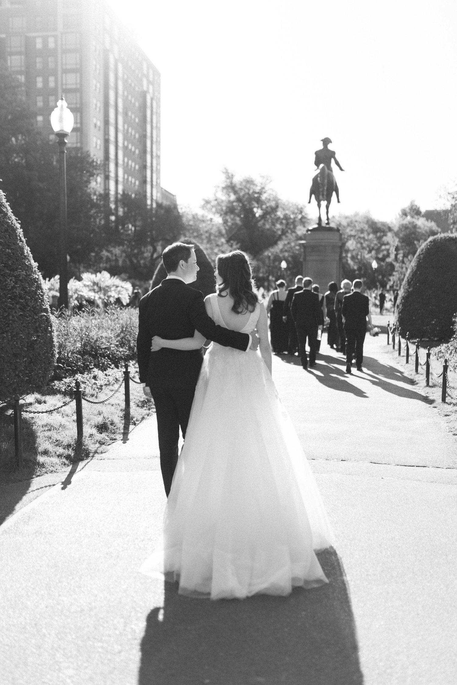 A wedding couple walks arm in arm with a statue silhouetted in the background.