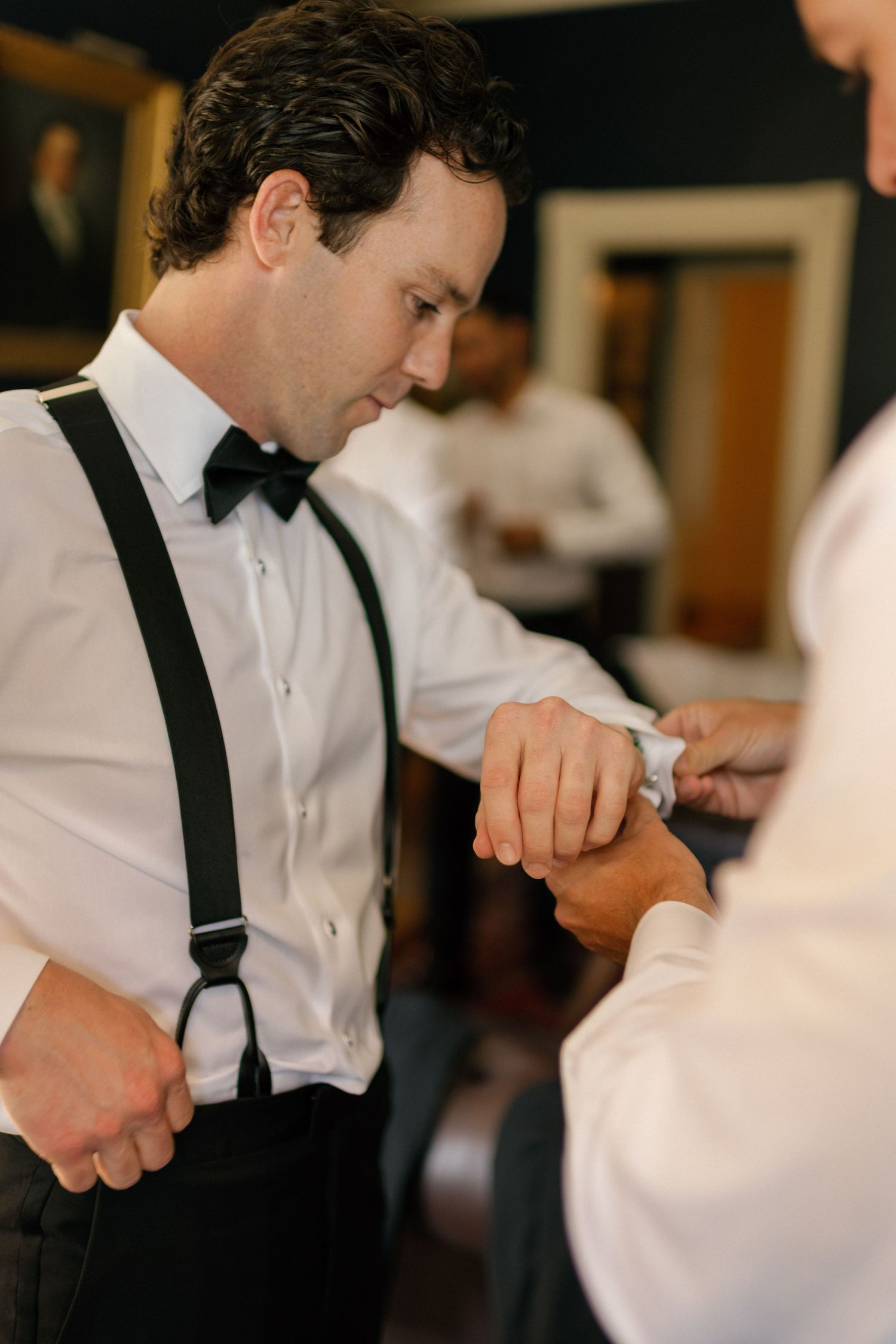 Person in formal attire with suspenders and bowtie checking time during event.