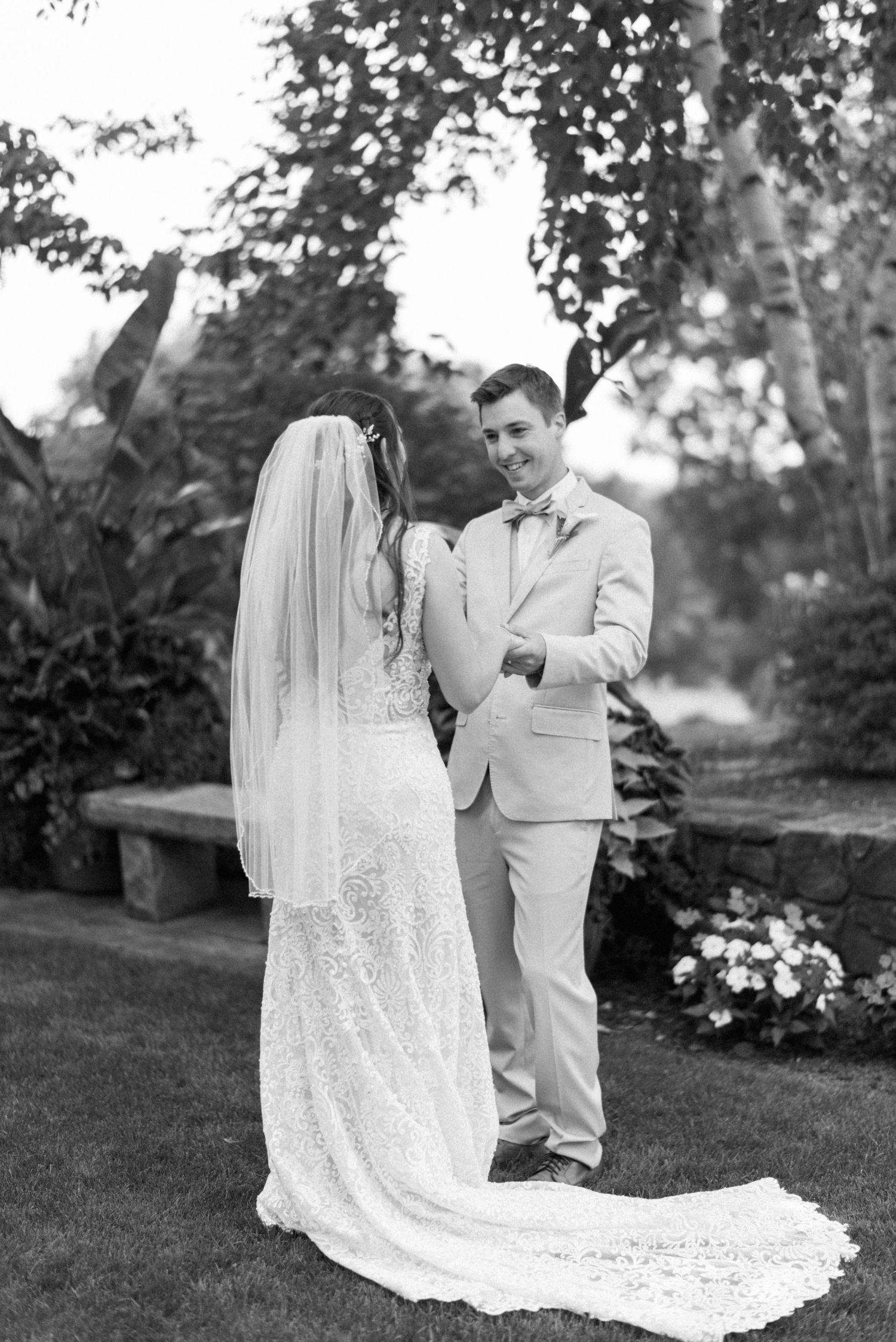 Black and white wedding portrait of couple in elegant attire standing outdoors.