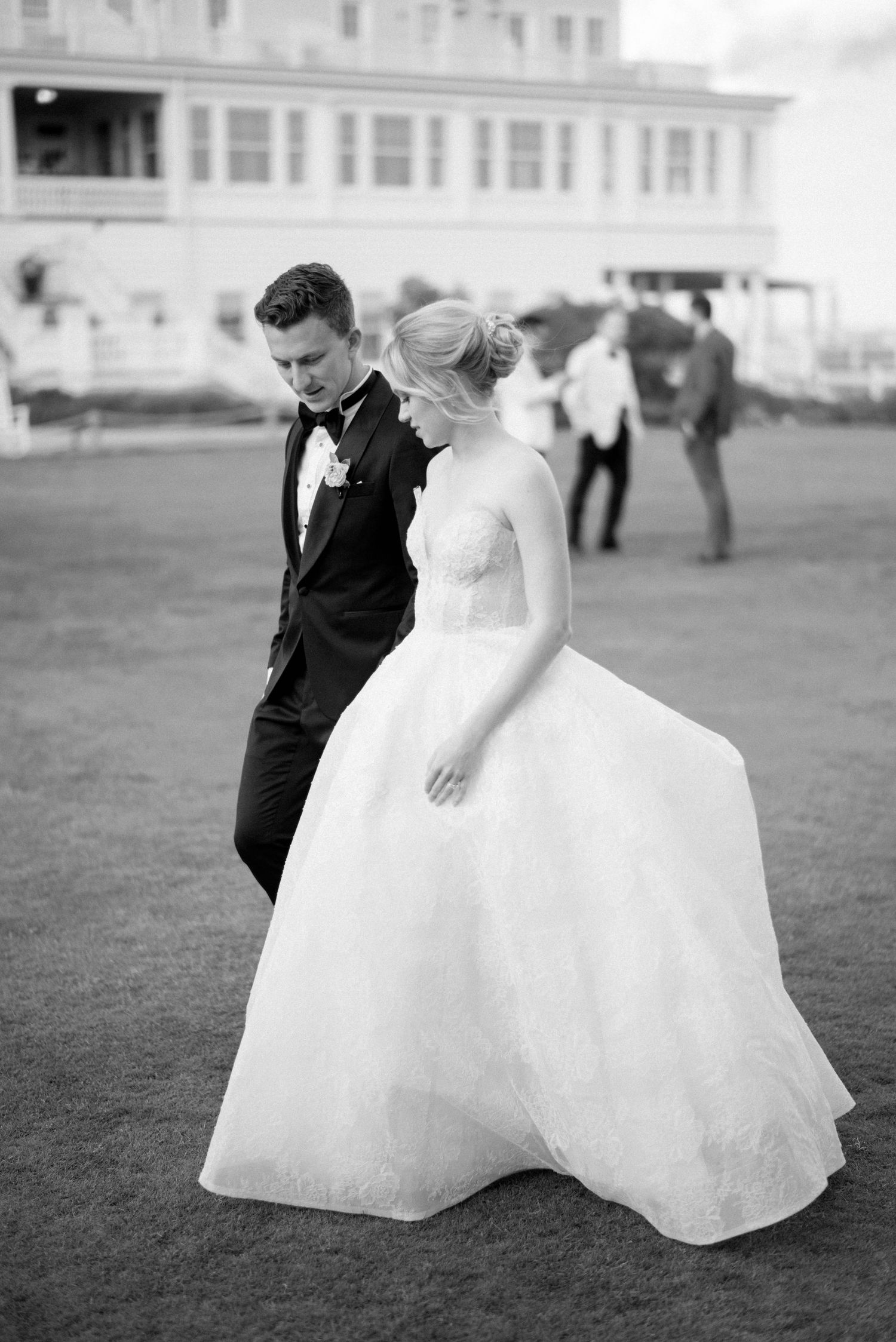 A couple in wedding attire sits together on a grassy lawn in an elegant black and white photograph.