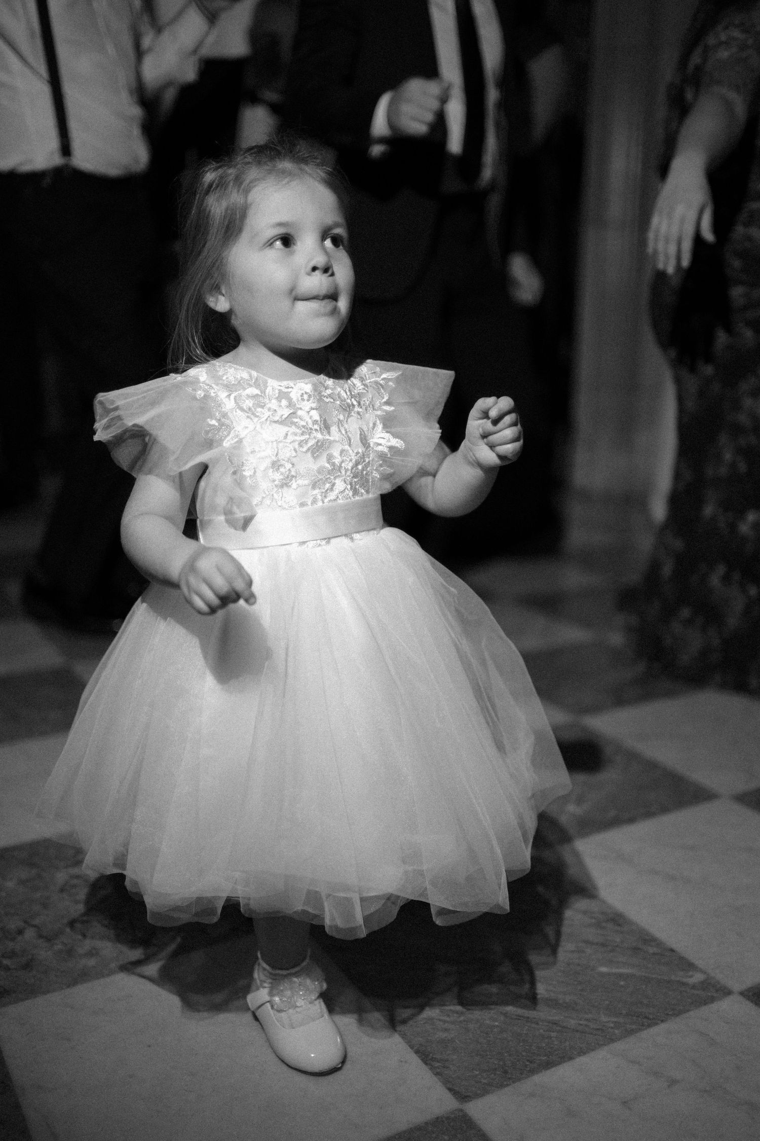 A small child in a white tulle dress and shoes twirls on a dance floor in black and white photography.