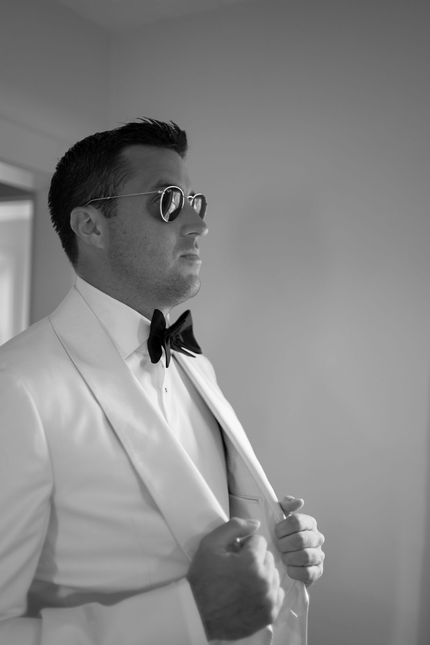 A man in a white suit and black bow tie adjusts his collar in a series of black and white photographs.