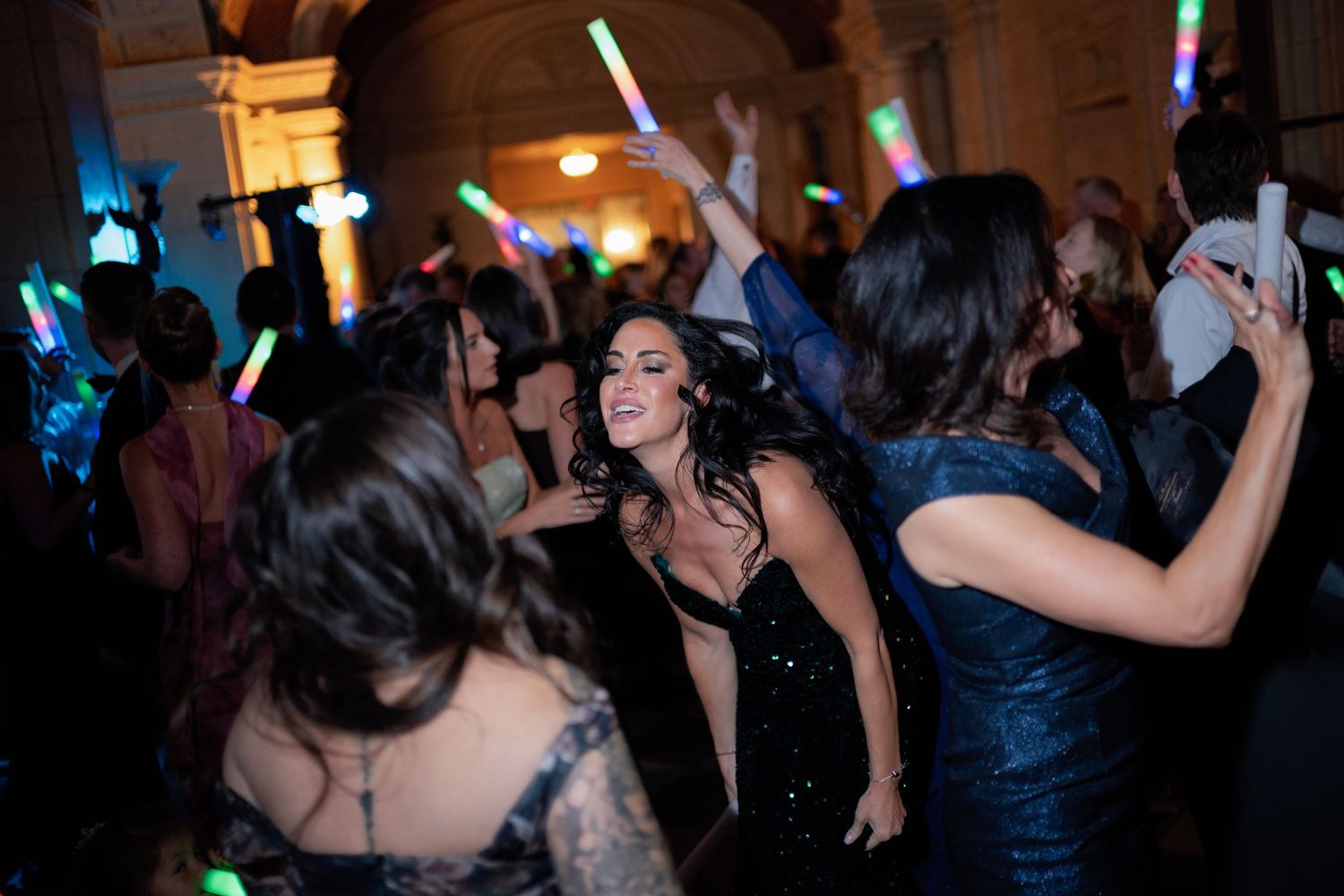 People dancing and enjoying themselves at a dimly lit party or nightclub with colorful lights in the background.
