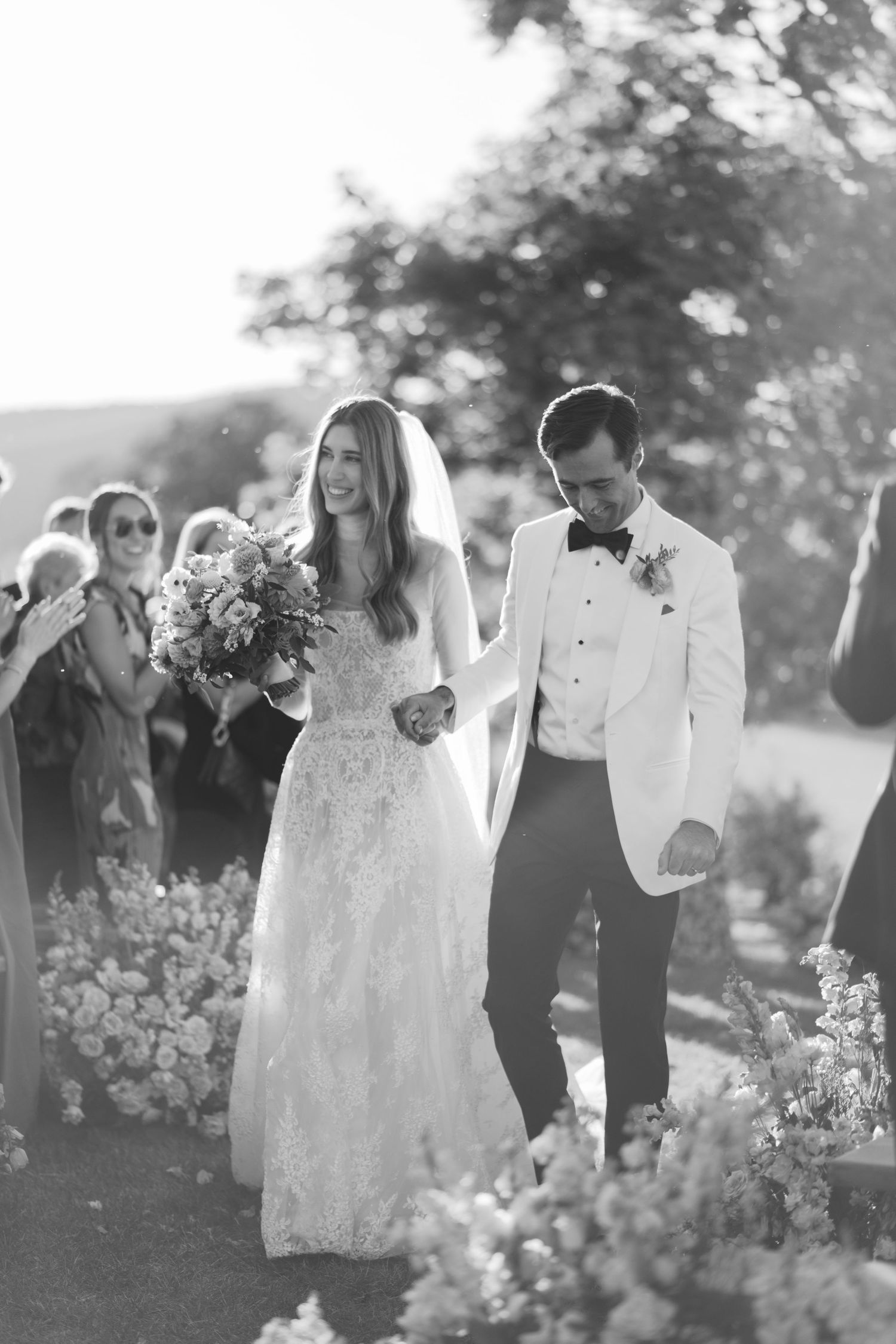 Black and white wedding photo of couple walking through garden path.