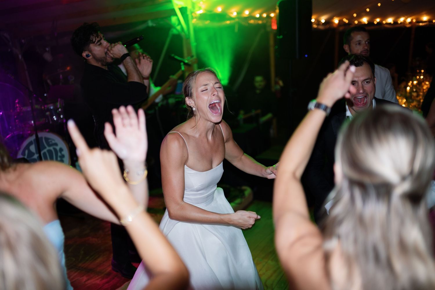 Bride dancing joyfully at wedding reception with live band and green lights.