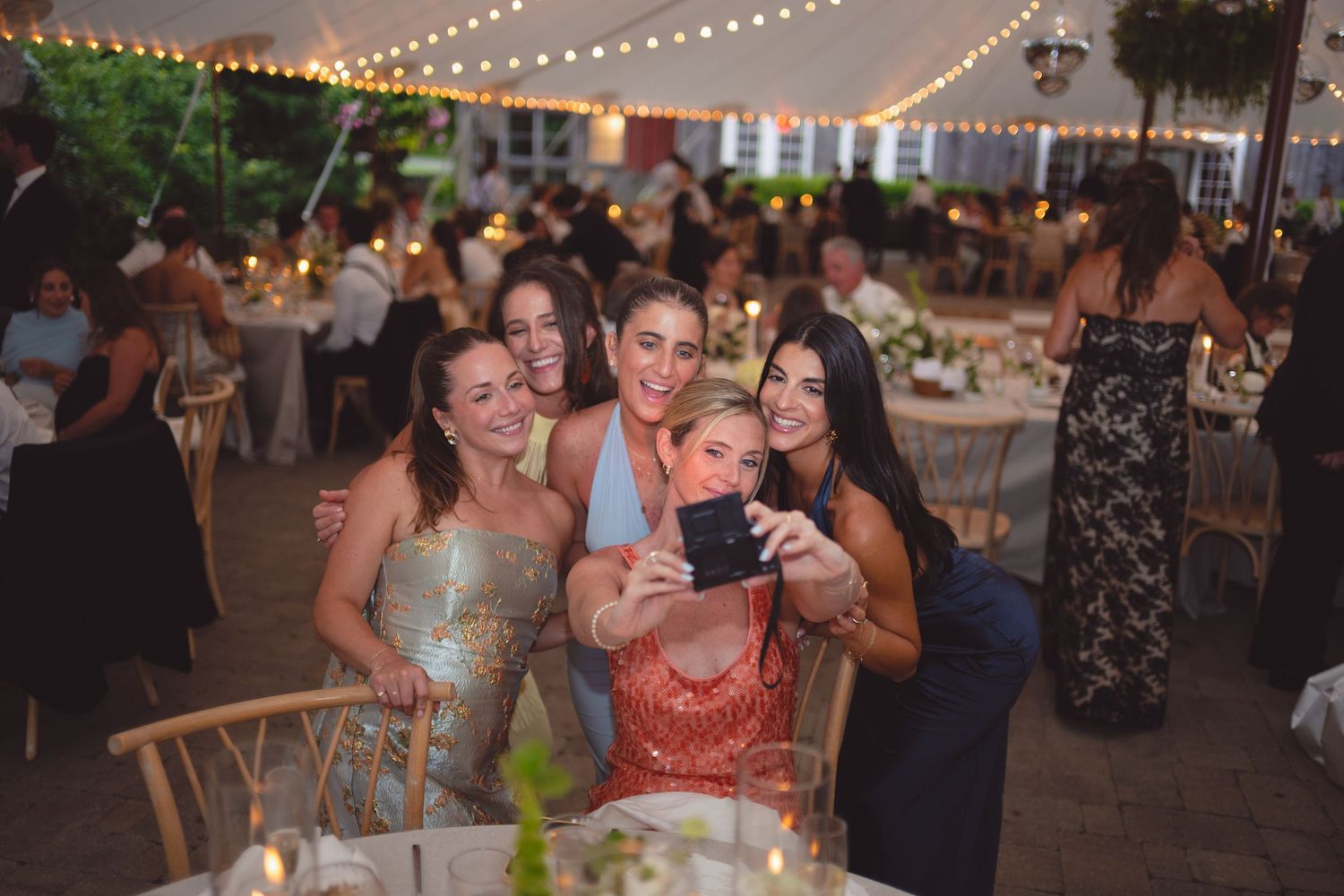 People dancing and celebrating at an outdoor evening reception under string lights and tents.