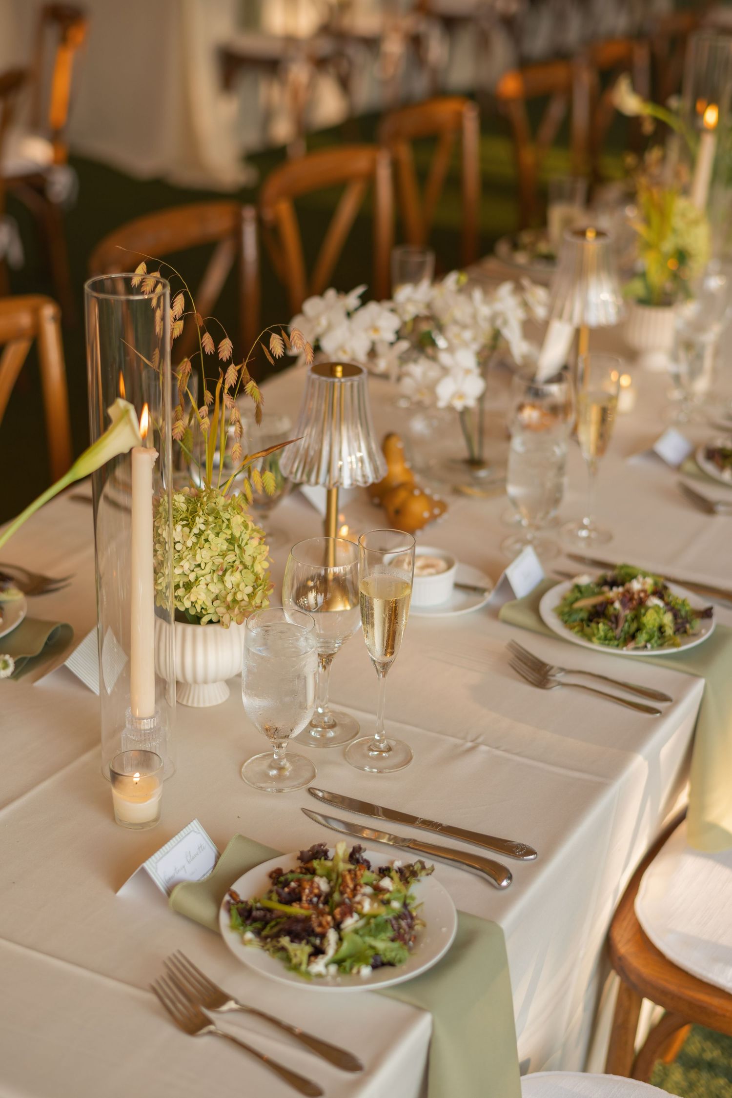 Elegant wedding reception table with white linens, candles, floral centerpieces, champagne flutes, and plated salads.