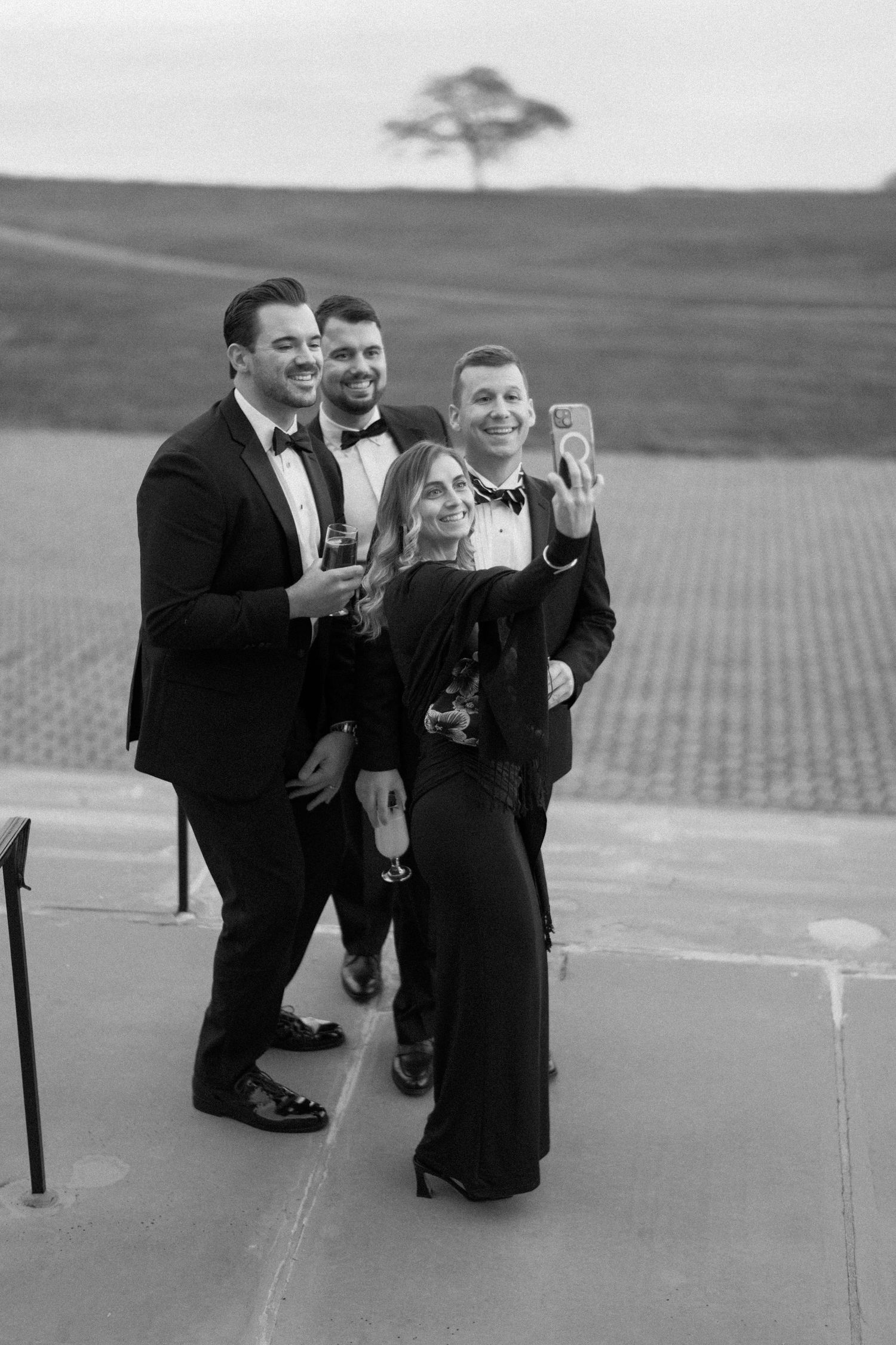 A series of black and white photos showing people in formal attire posing playfully on a sidewalk with fields in background.