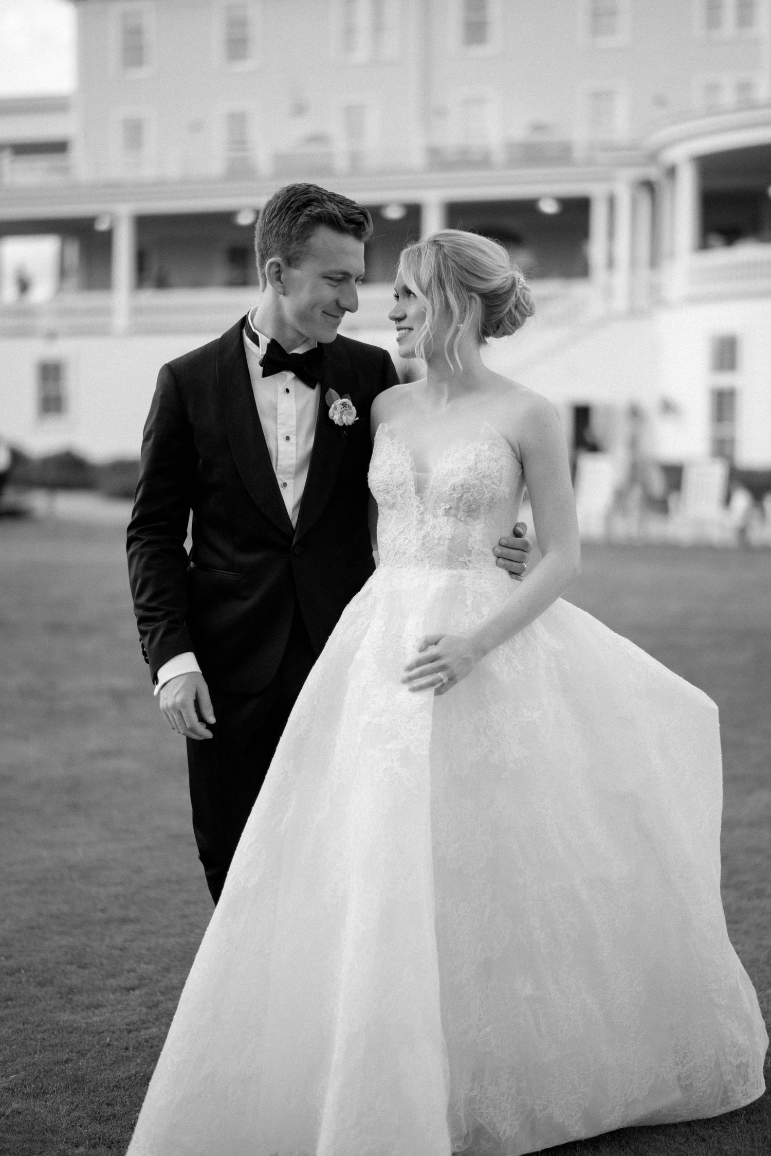 A couple in formal wedding attire share a romantic moment together on a grassy lawn.