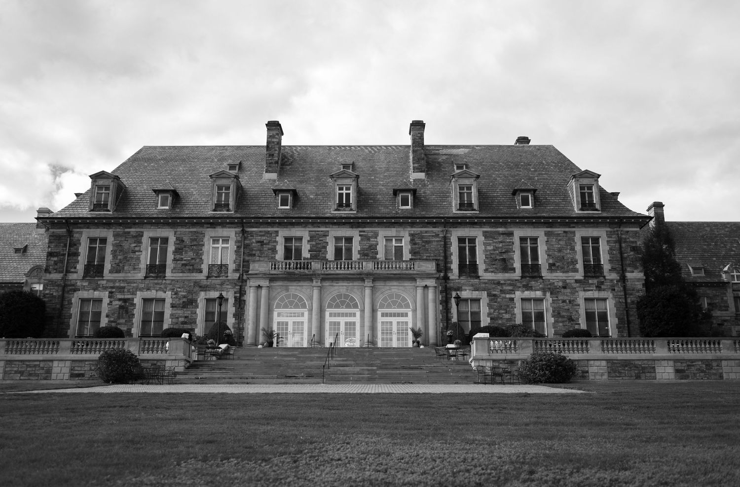 Historic stone manor house with symmetrical architecture and multiple chimneys shown in black and white panoramic view.