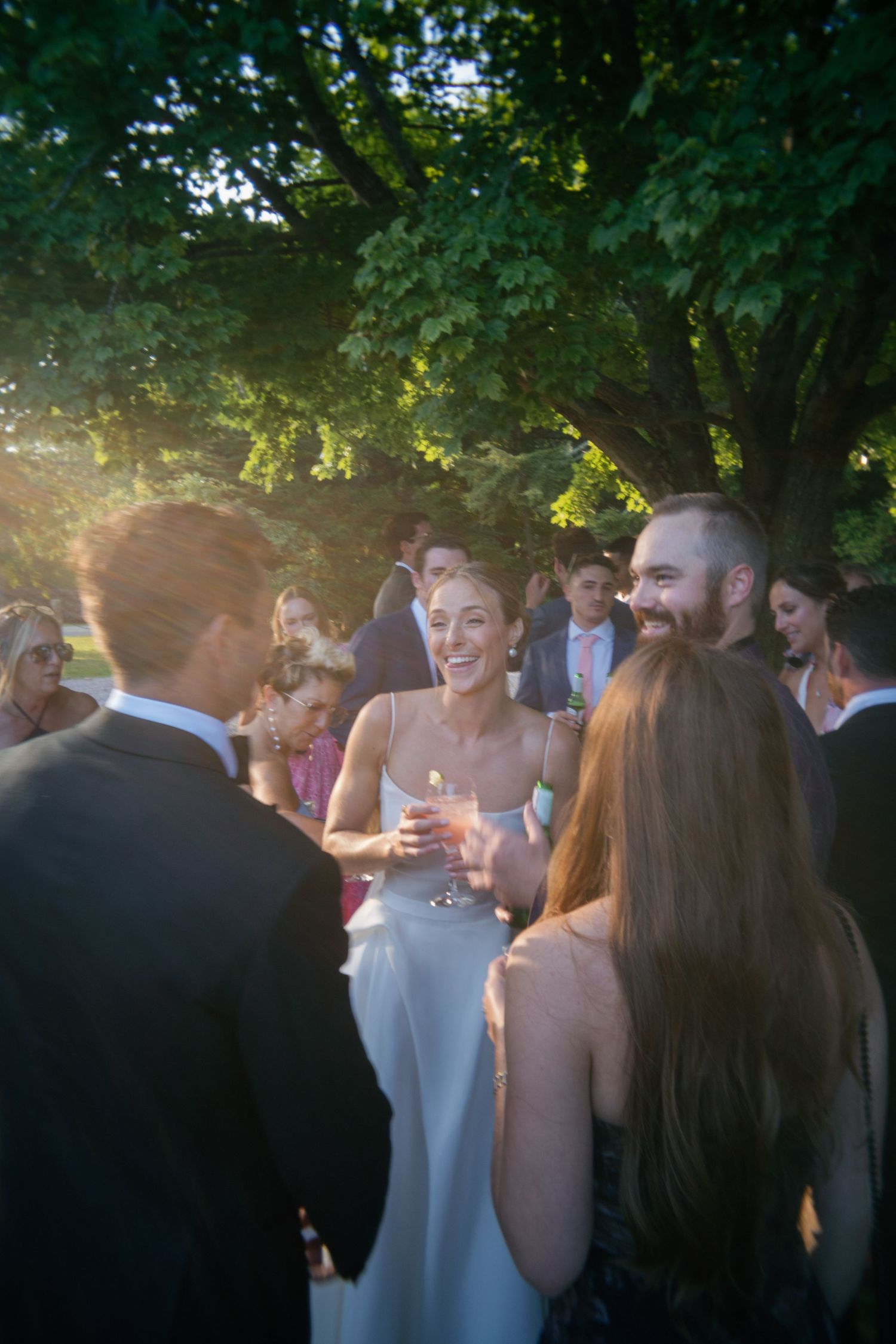 Bride in white gown laughing with guests at an outdoor wedding reception during golden hour.
