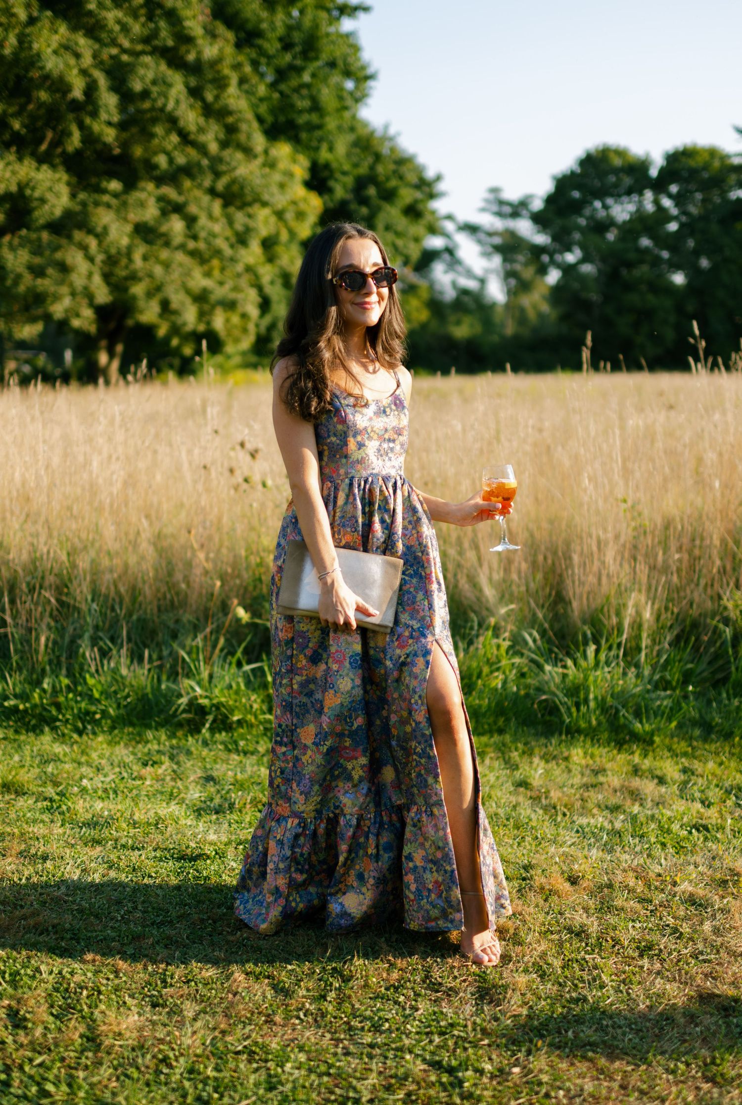Summer portrait of a person in a floral maxi dress holding a cocktail in a golden field.