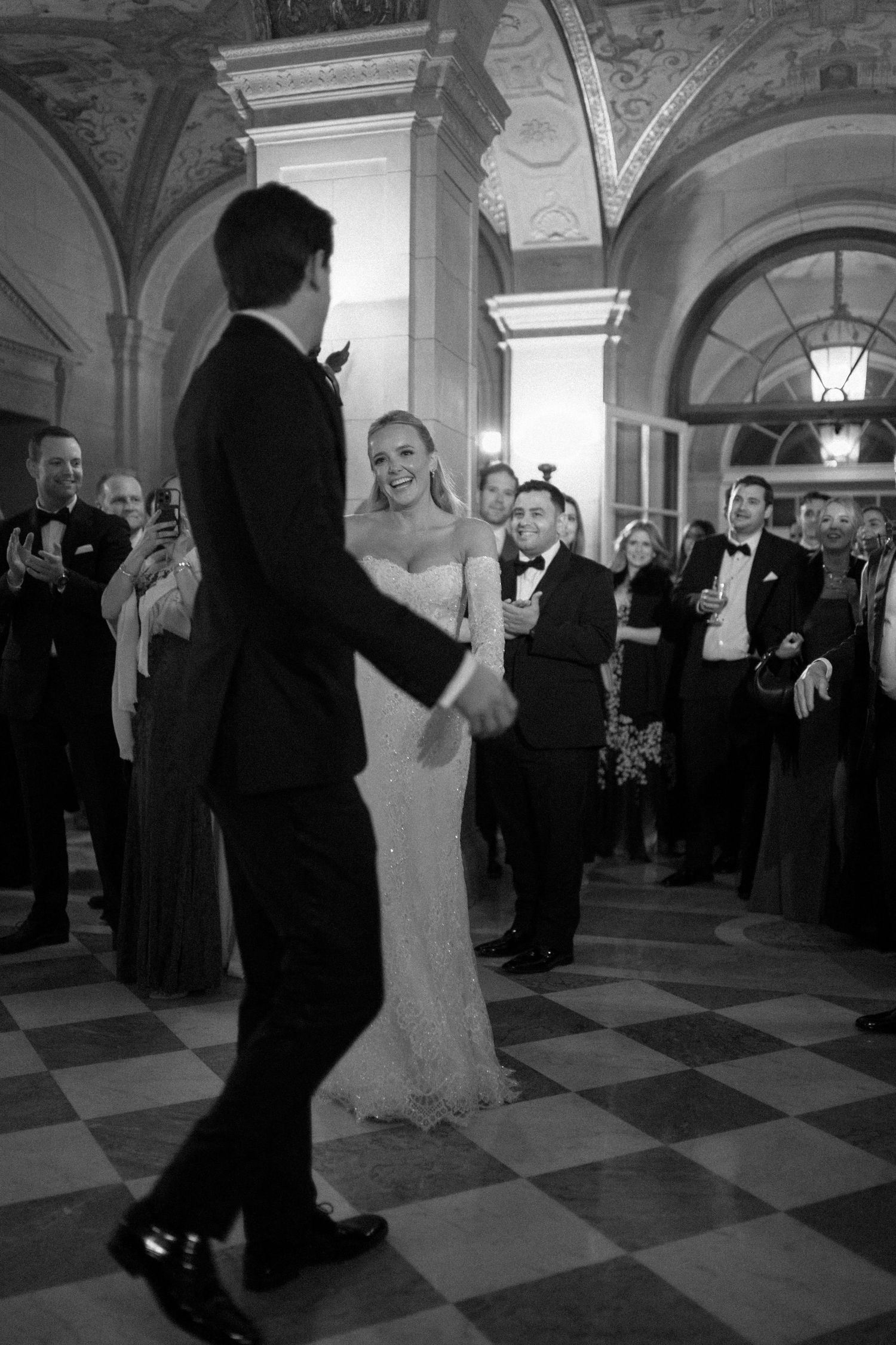 A couple shares their first dance at a wedding reception in an elegant ballroom with checkerboard floors.