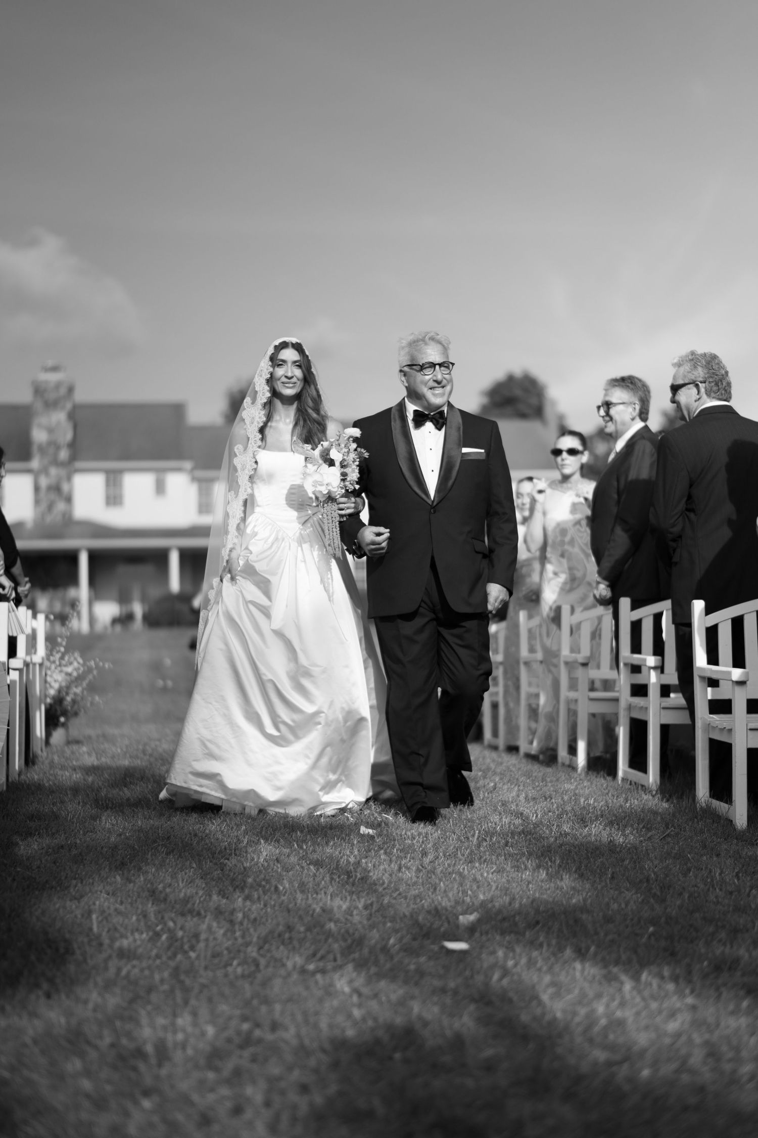 A bride and groom walk together on a grassy hillside in black and white photography.