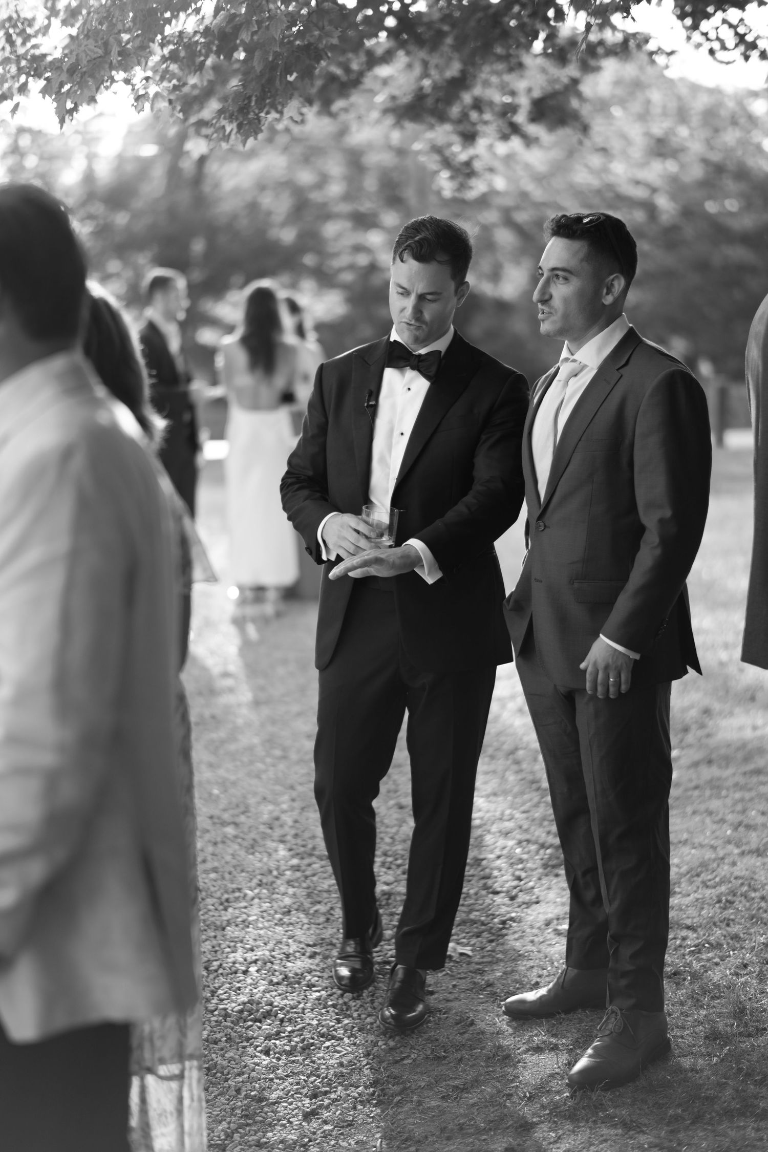 Two men in suits converse outdoors at a wedding reception in this elegant black and white photo.