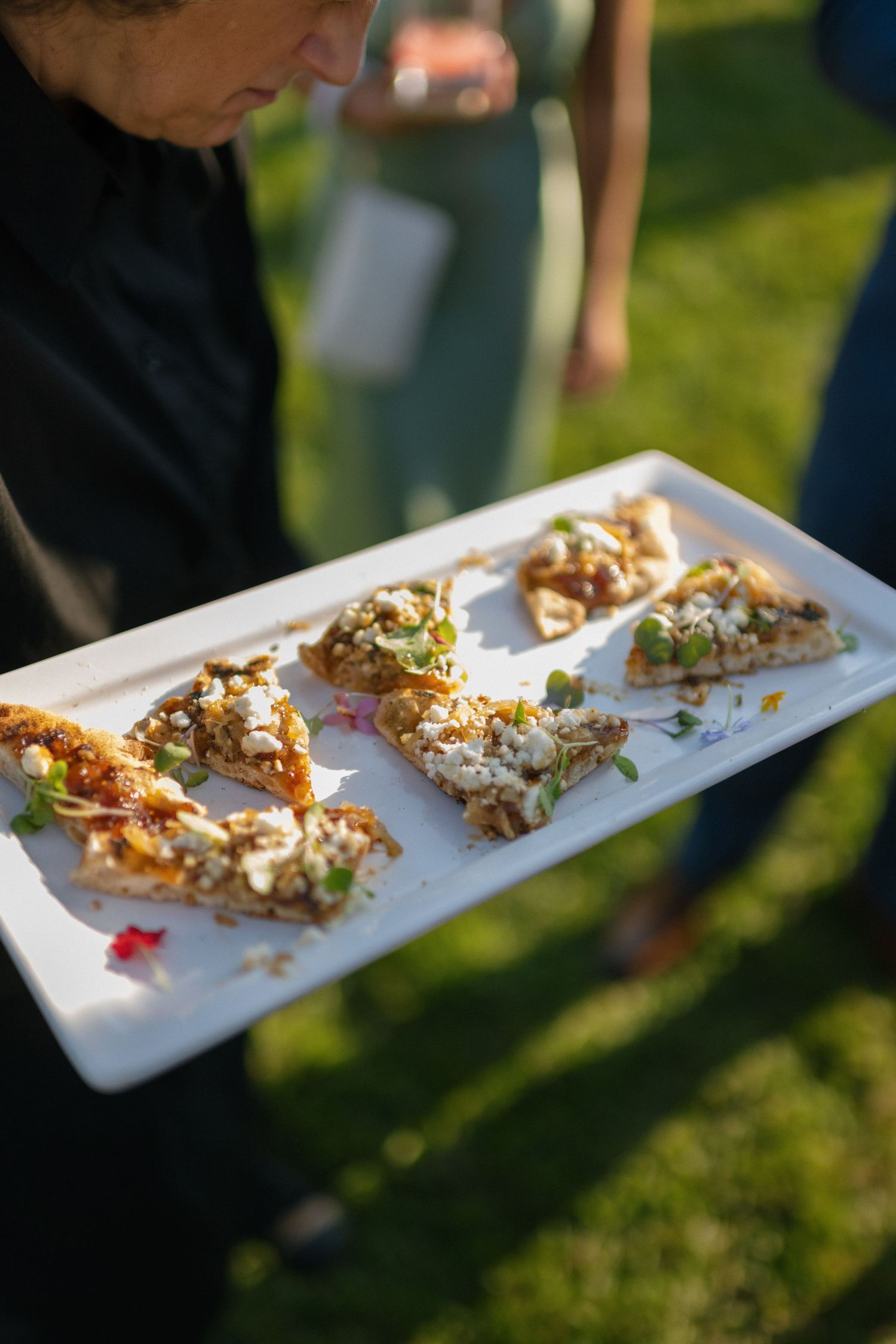 Elegant appetizers being served on a white platter at an outdoor wedding reception.