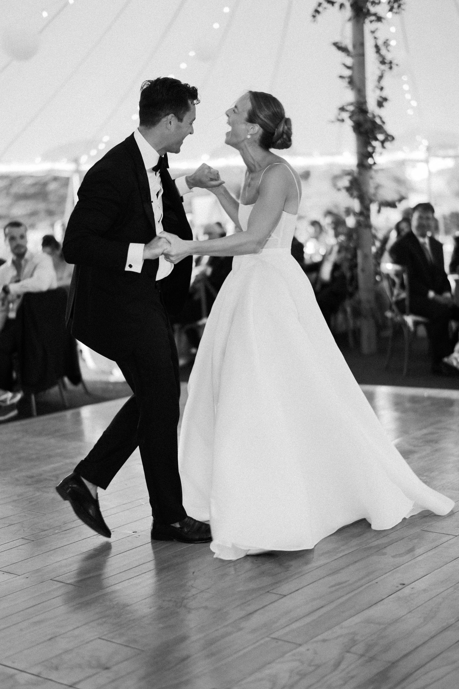 Black and white photo of a bride and groom sharing their first dance under a tent at their wedding reception.