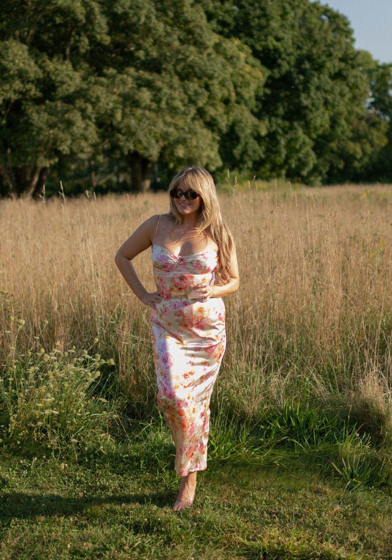 Floral dress in a sunny meadow with tall grass and trees in the background.