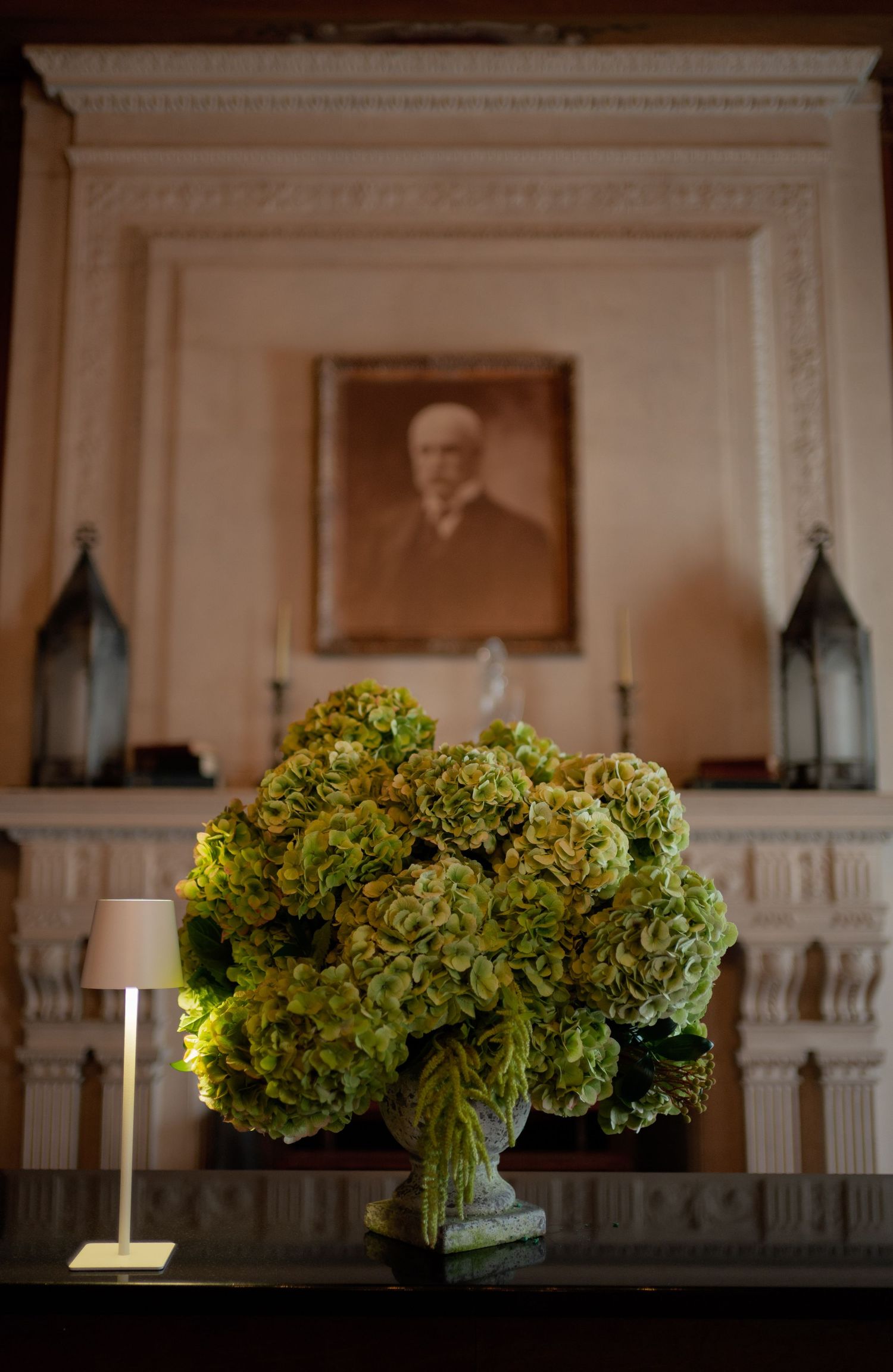 Green hydrangea floral arrangements sit atop white mantels in an elegant room with classic architectural details.