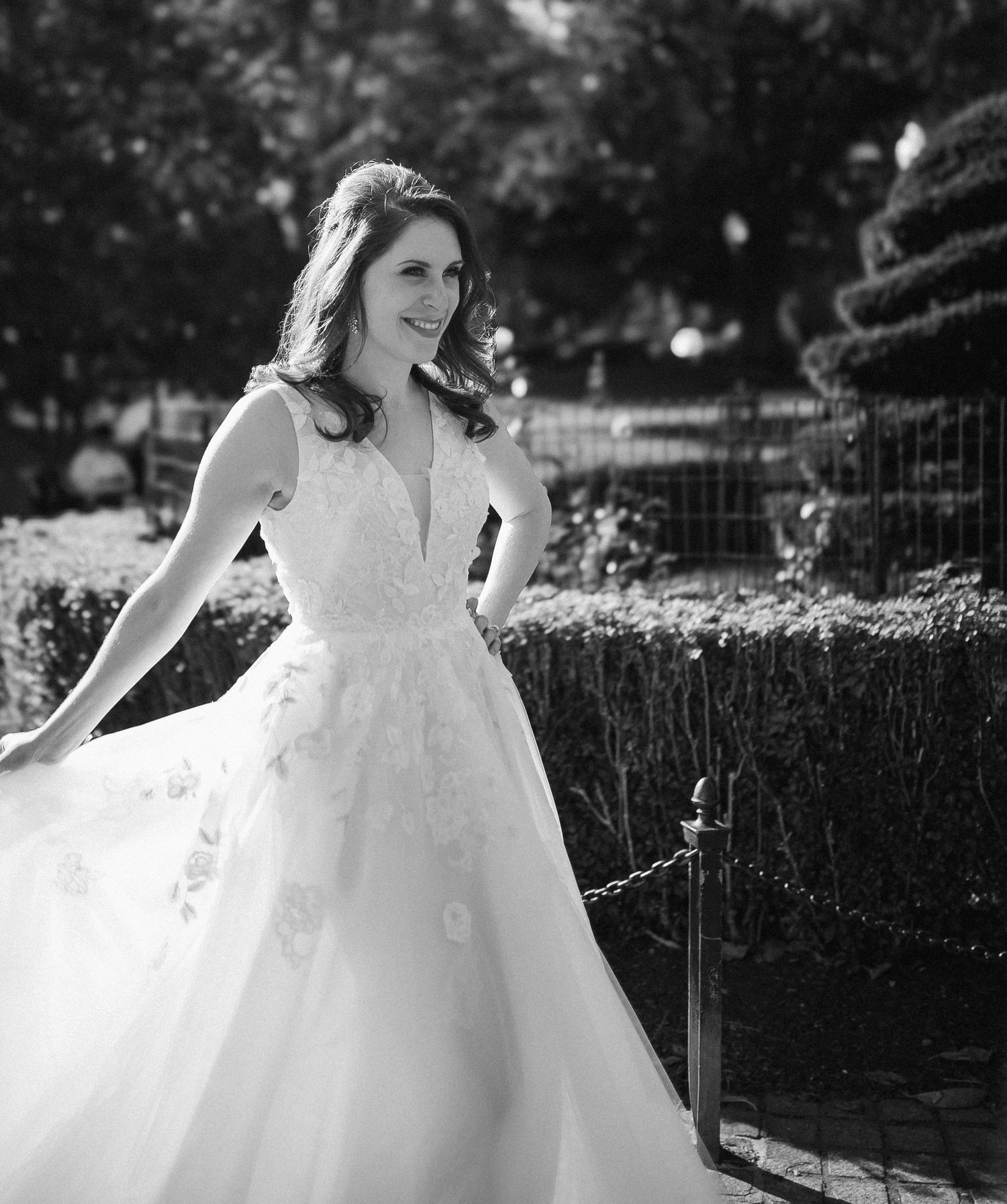 Bride in a floral ballgown wedding dress poses gracefully in a garden setting, black and white photo.
