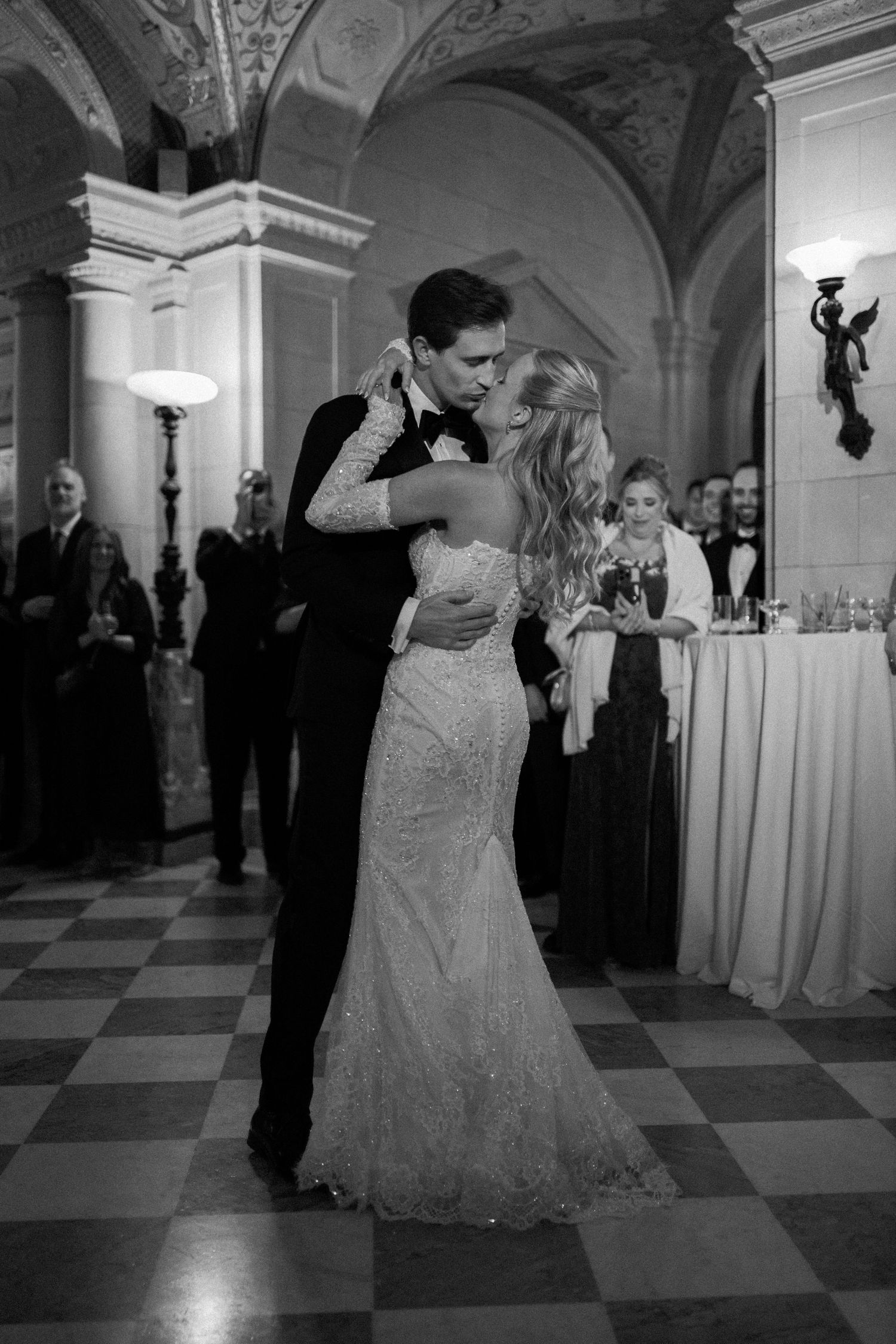 A couple performs an elegant dance dip in a grand ballroom with checkerboard floors and ornate architecture.