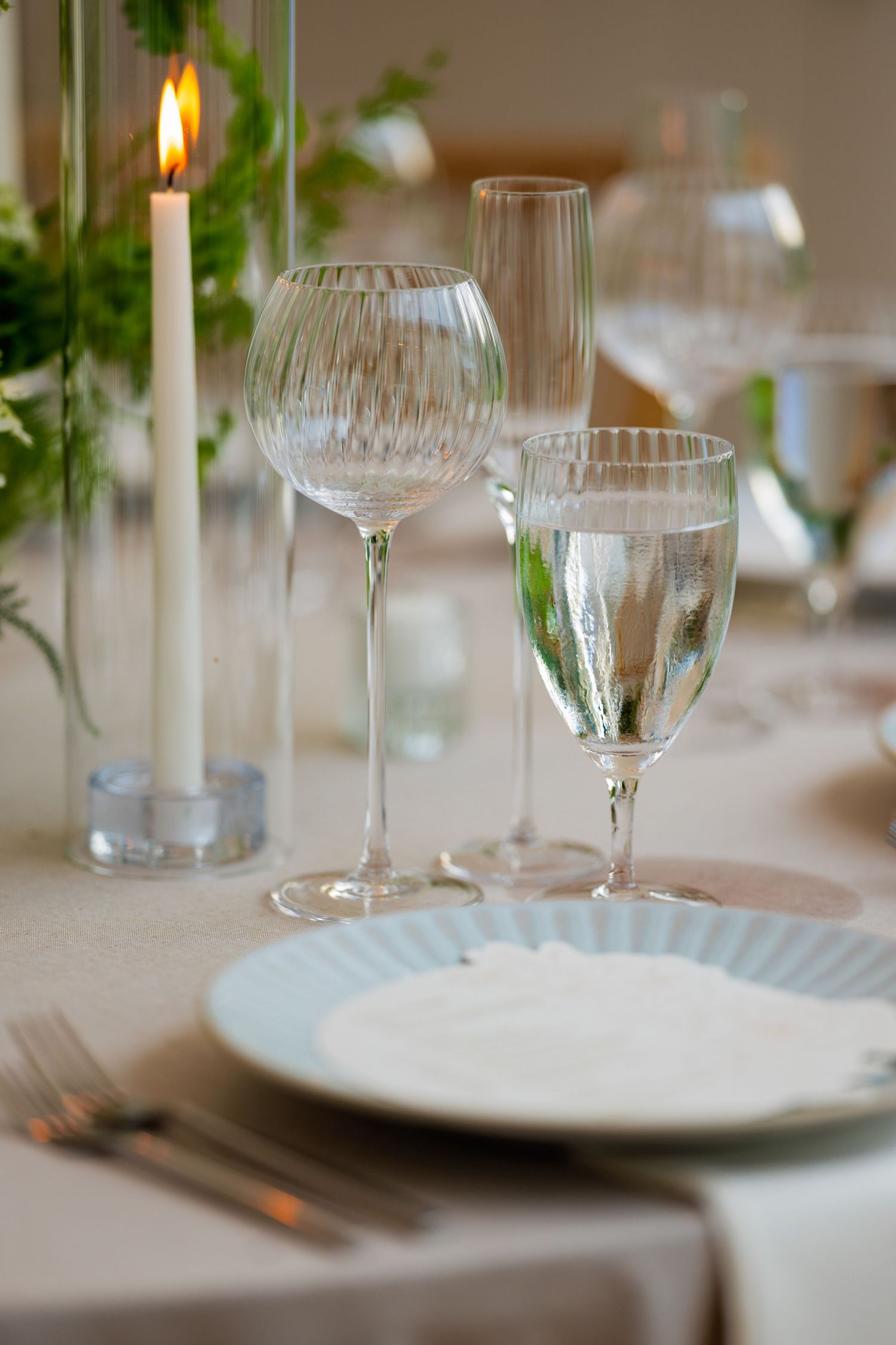 Elegant table setting with white plates, wine glasses, and lit candles creating a romantic dining atmosphere.