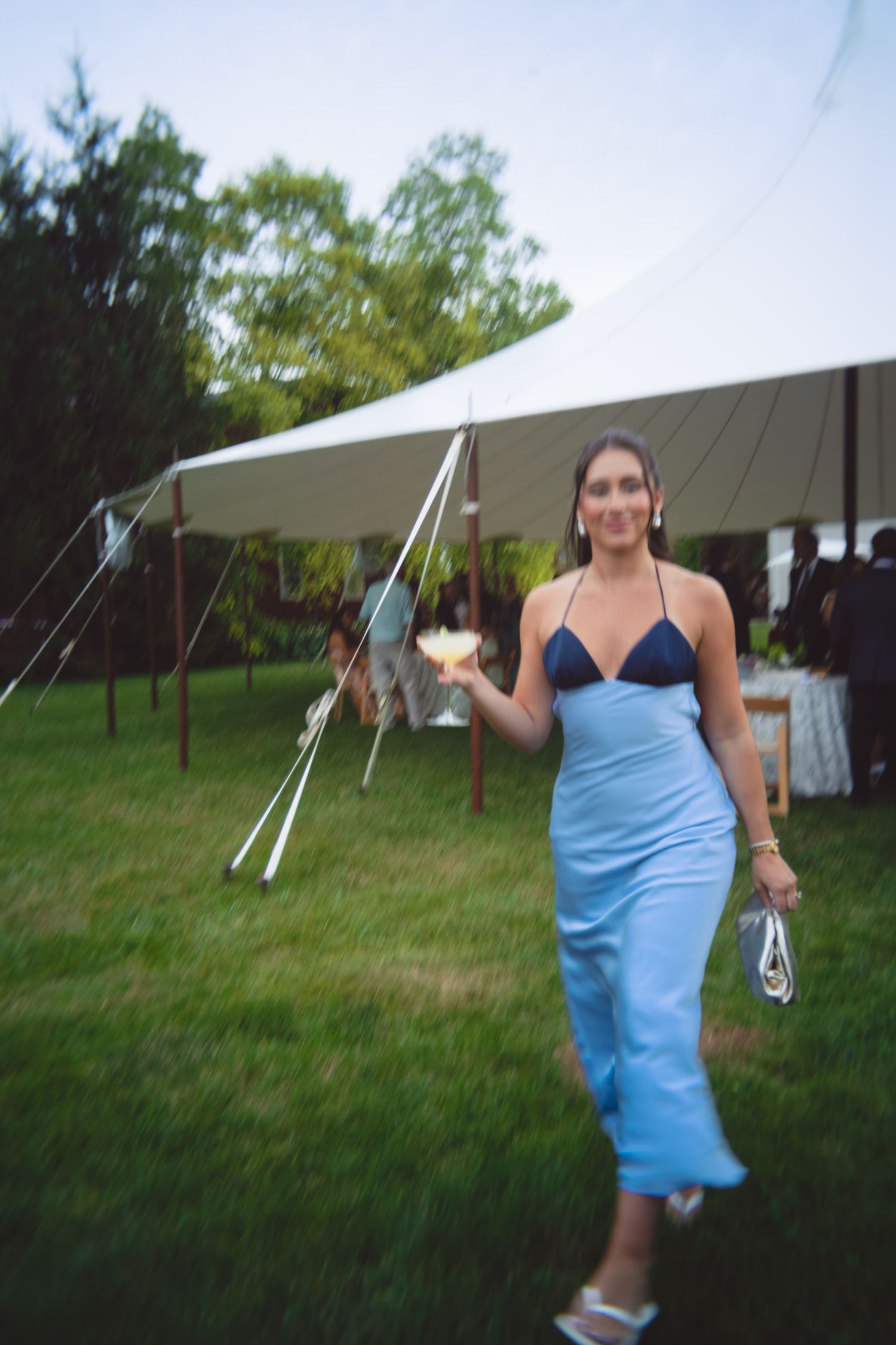 A sequence of someone in a blue dress spinning and dancing outdoors near a white tent on a grassy field.