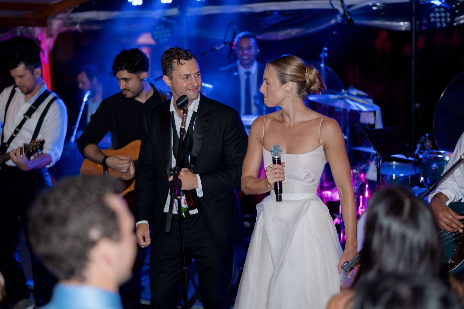 Bride and groom singing with microphones alongside live band at elegant wedding reception.
