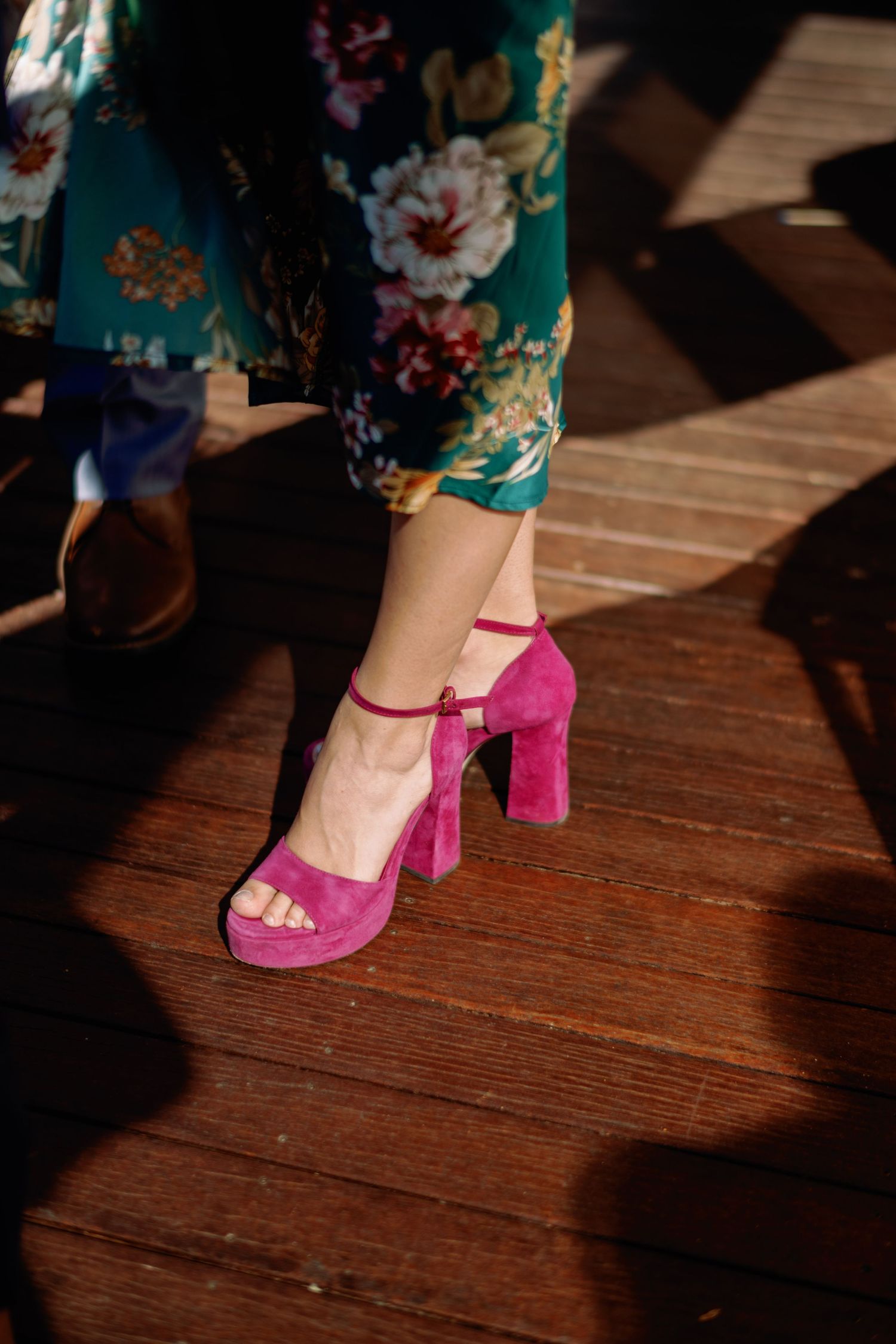 Pink velvet platform sandals and floral pants captured in dramatic lighting on wooden floor.