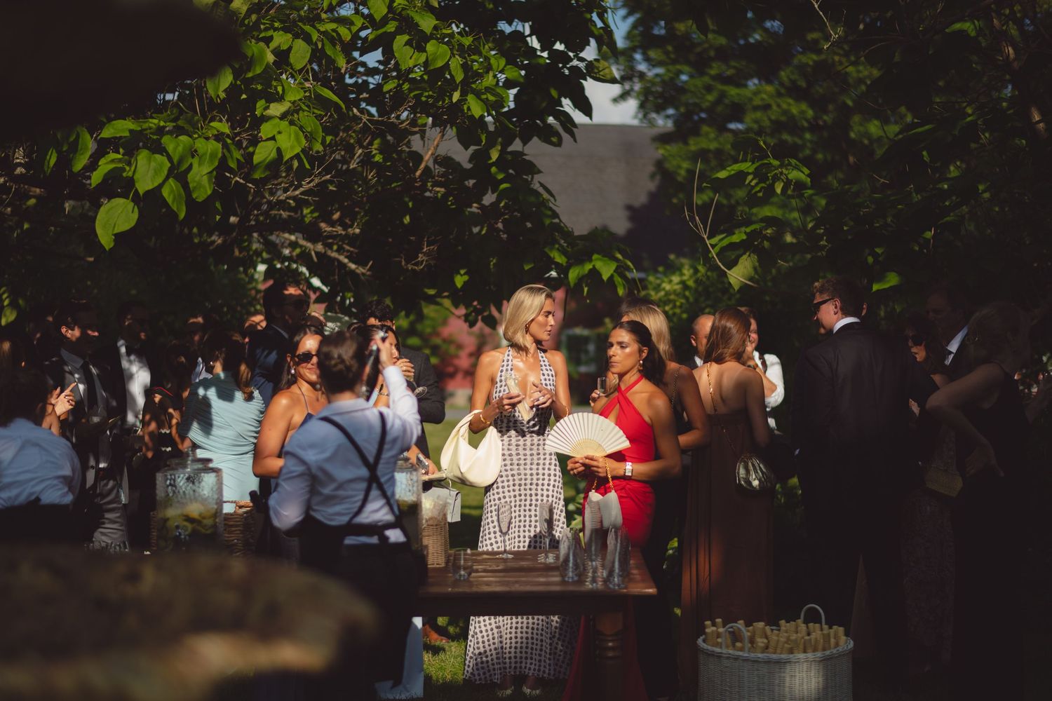 A dark outdoor wedding reception at night with string lights illuminating guests mingling under trees and tents.