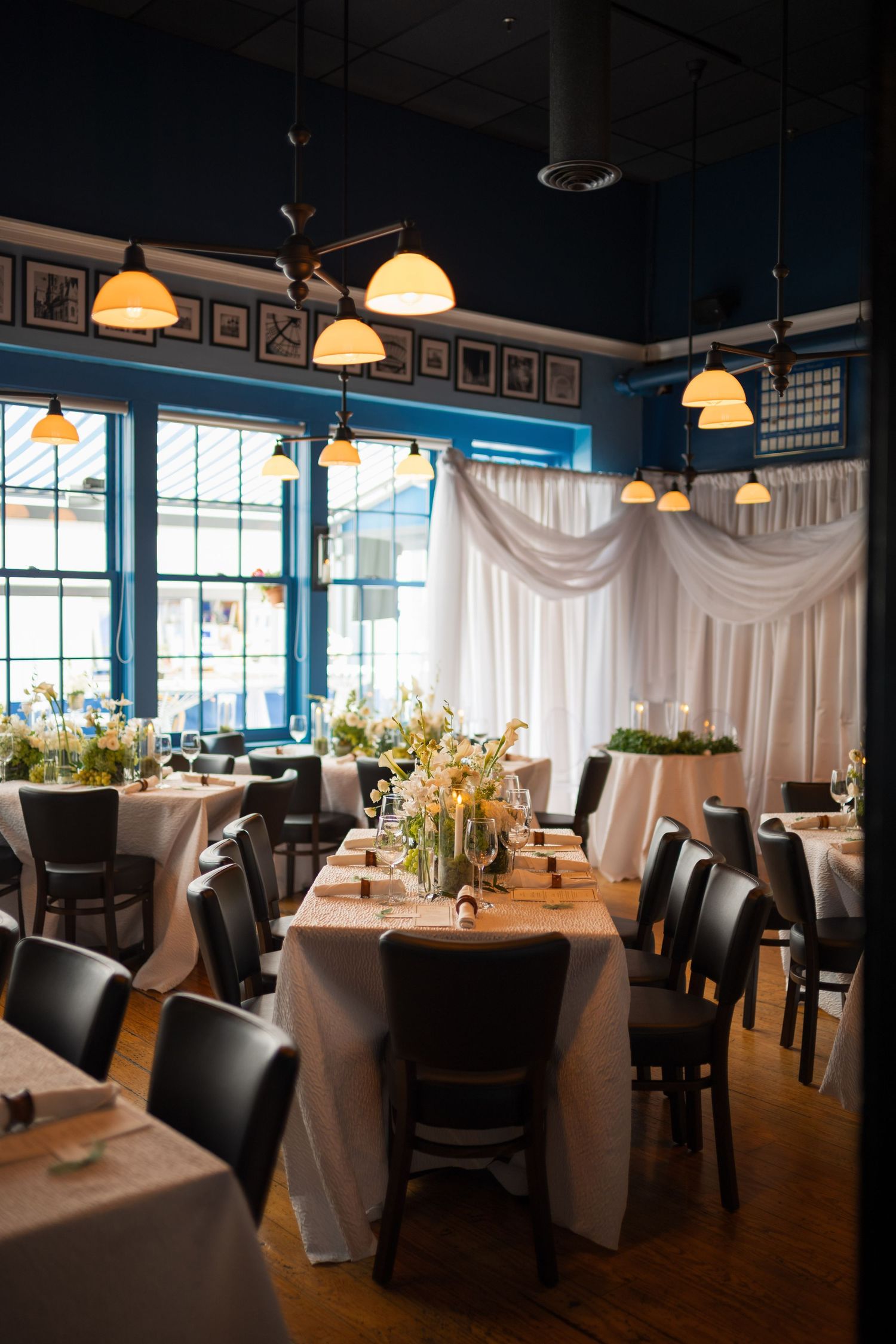 Elegant restaurant interior with white tablecloths, black leather chairs, and warm pendant lighting creates an upscale dining atmosphere.