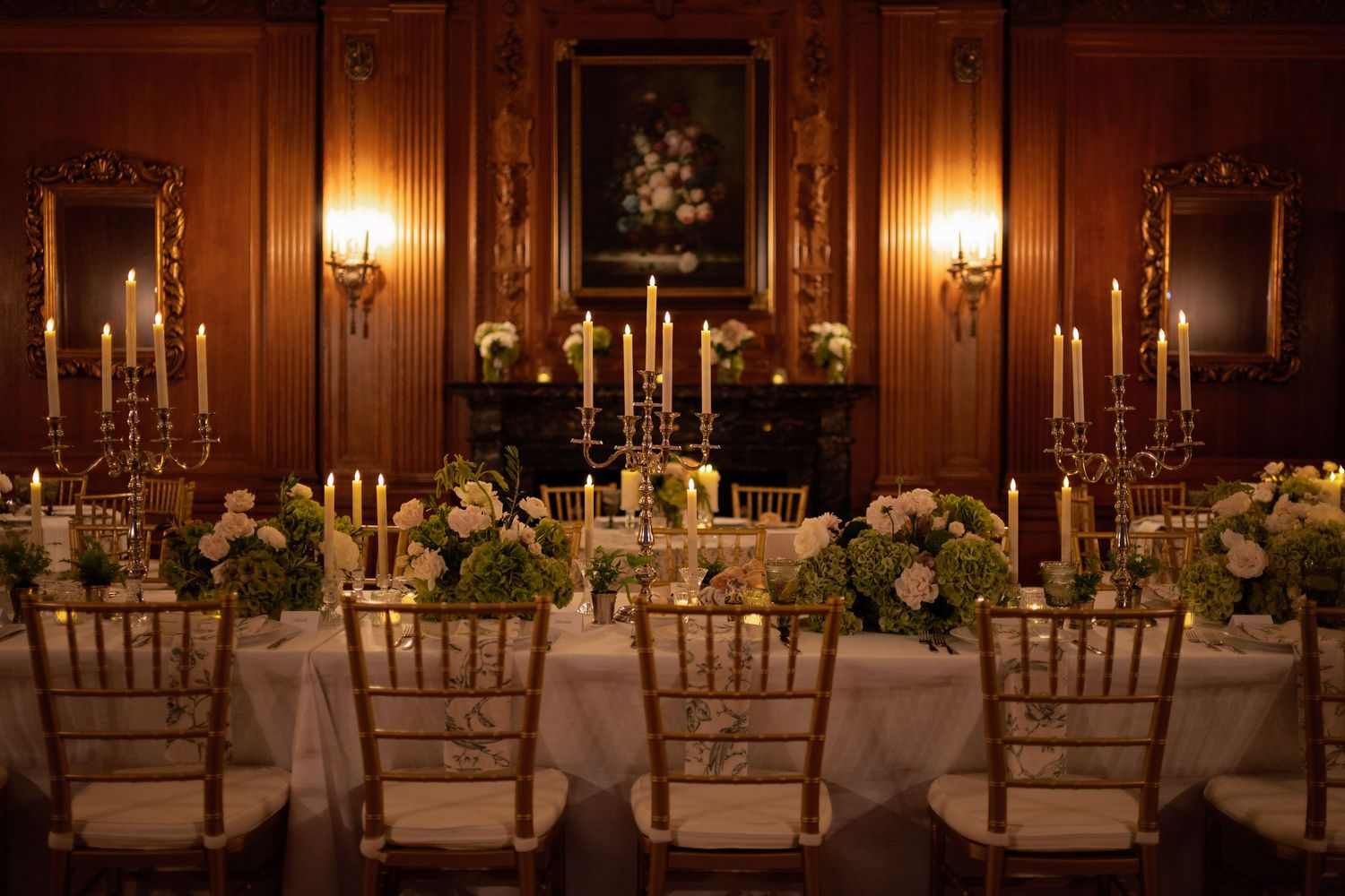Elegant candlelit reception tables adorned with white floral centerpieces and gold candelabras in a warm-lit ballroom.