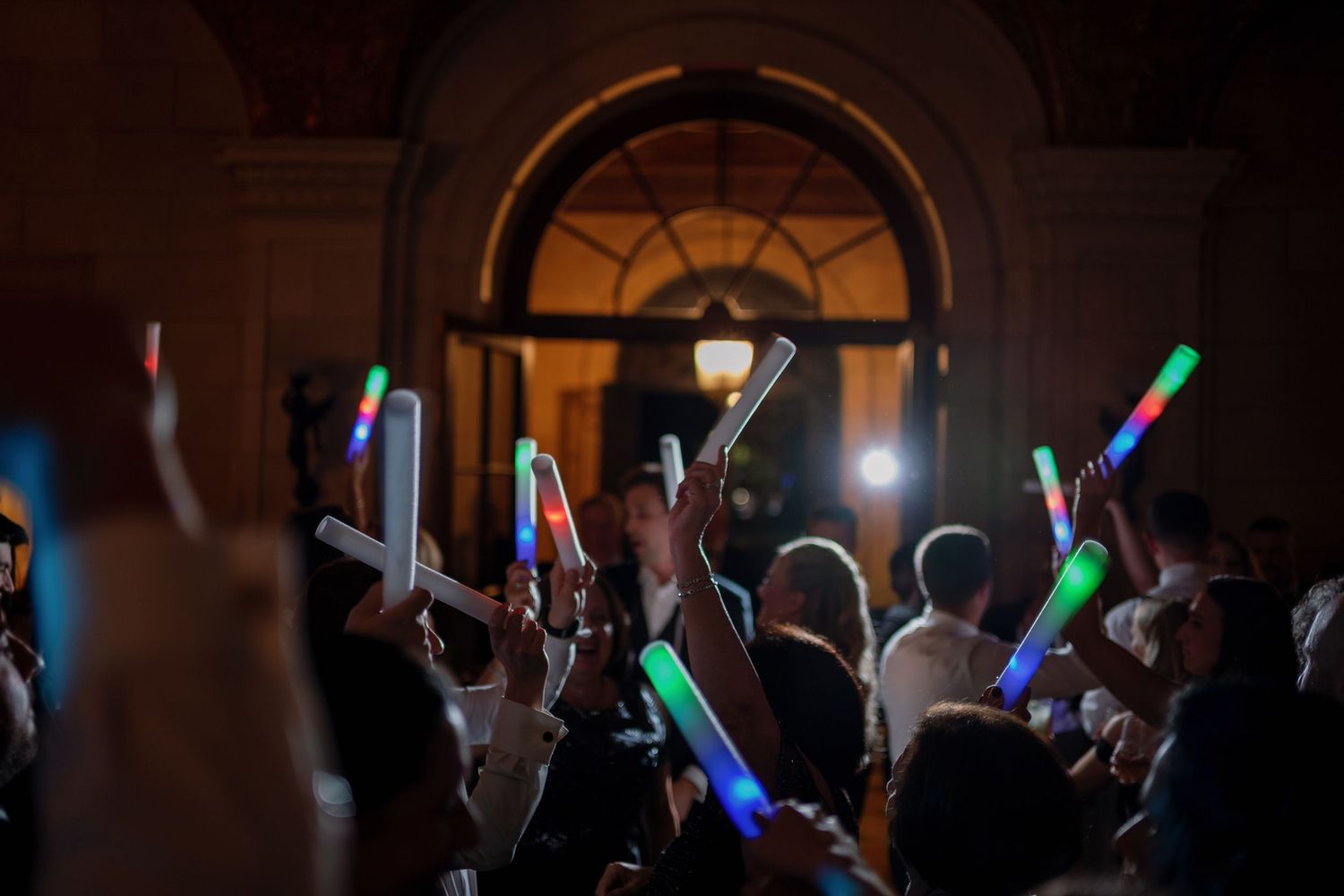 Concert crowd holds up glowing LED foam sticks in a dark venue during a performance.