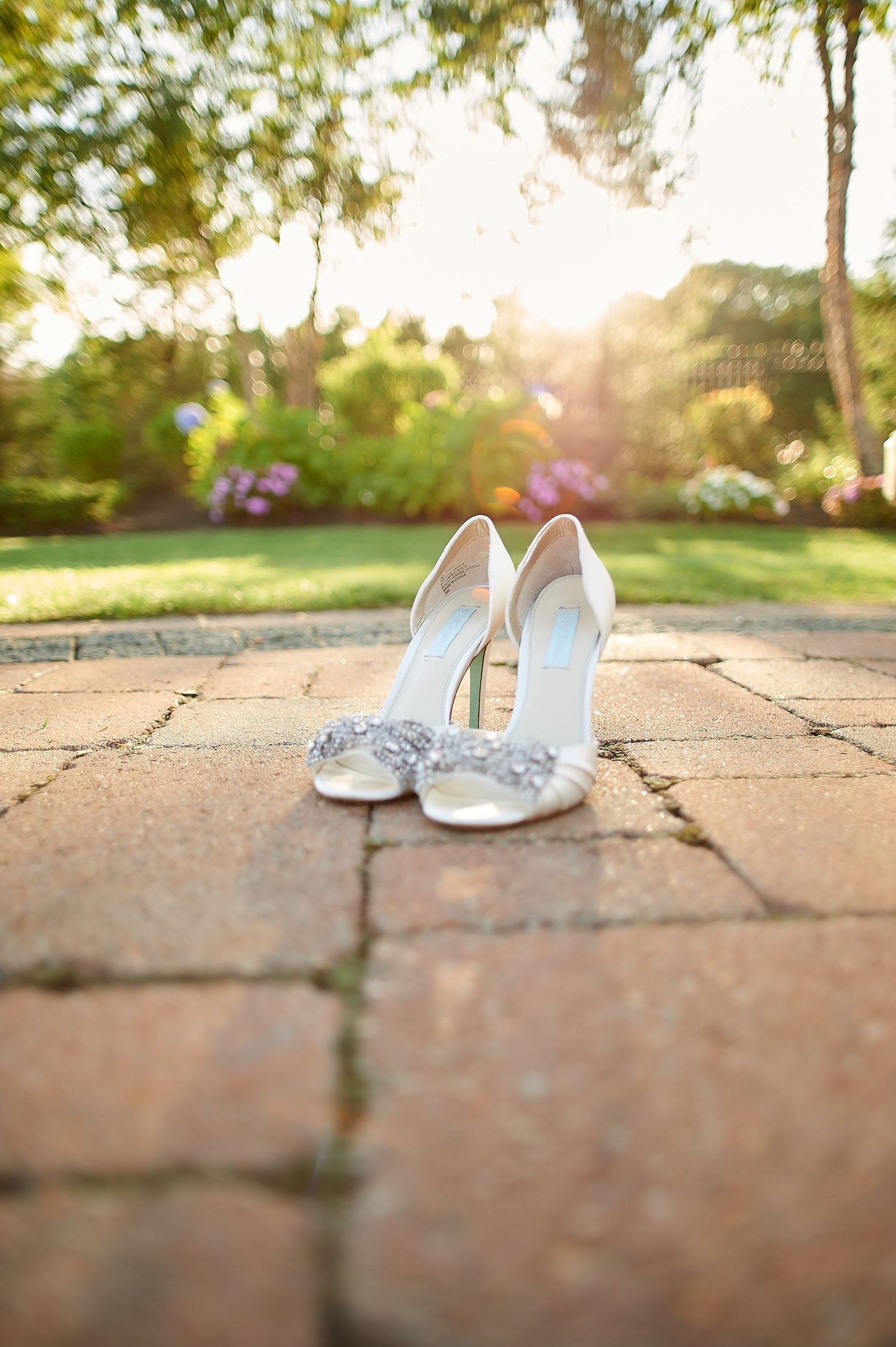 Embellished white bridal shoes on stone paving with sunset lighting in background.