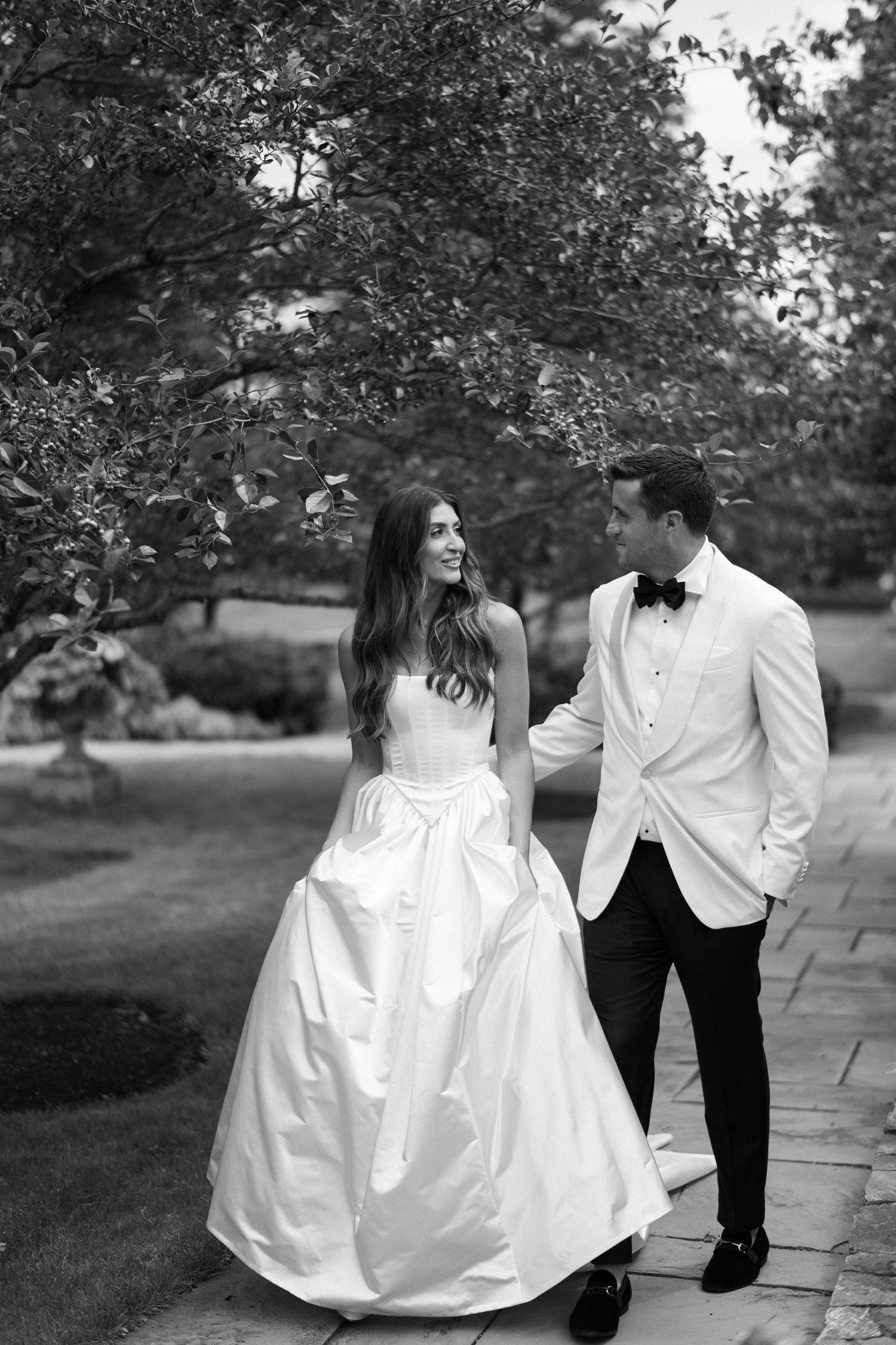 A romantic black and white photo sequence showing a couple in wedding attire walking and interacting along a path outdoors.